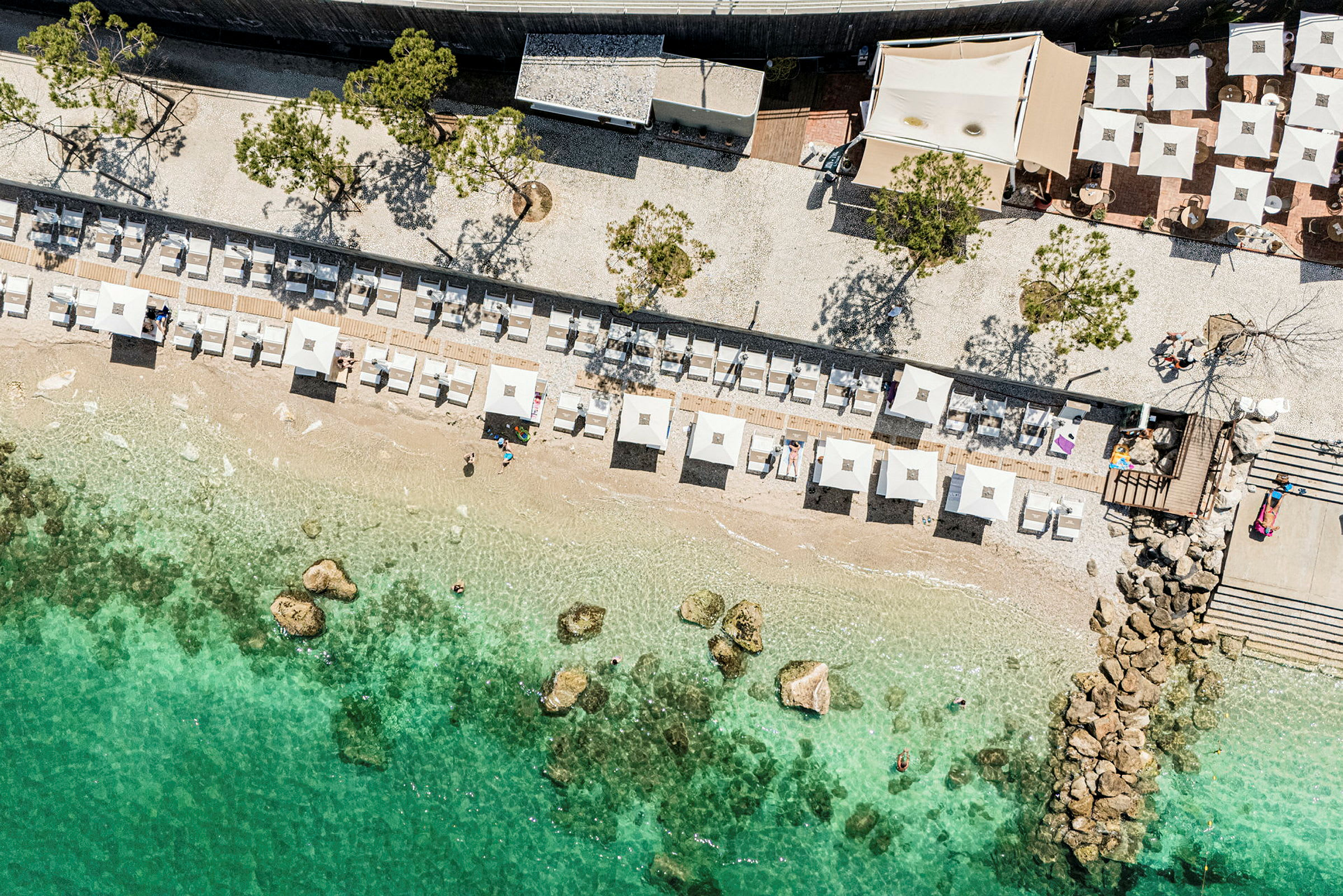 Flygfoto över en strand med parasoller och solstolar, samt klart, turkost vatten. (AI-genererad text)