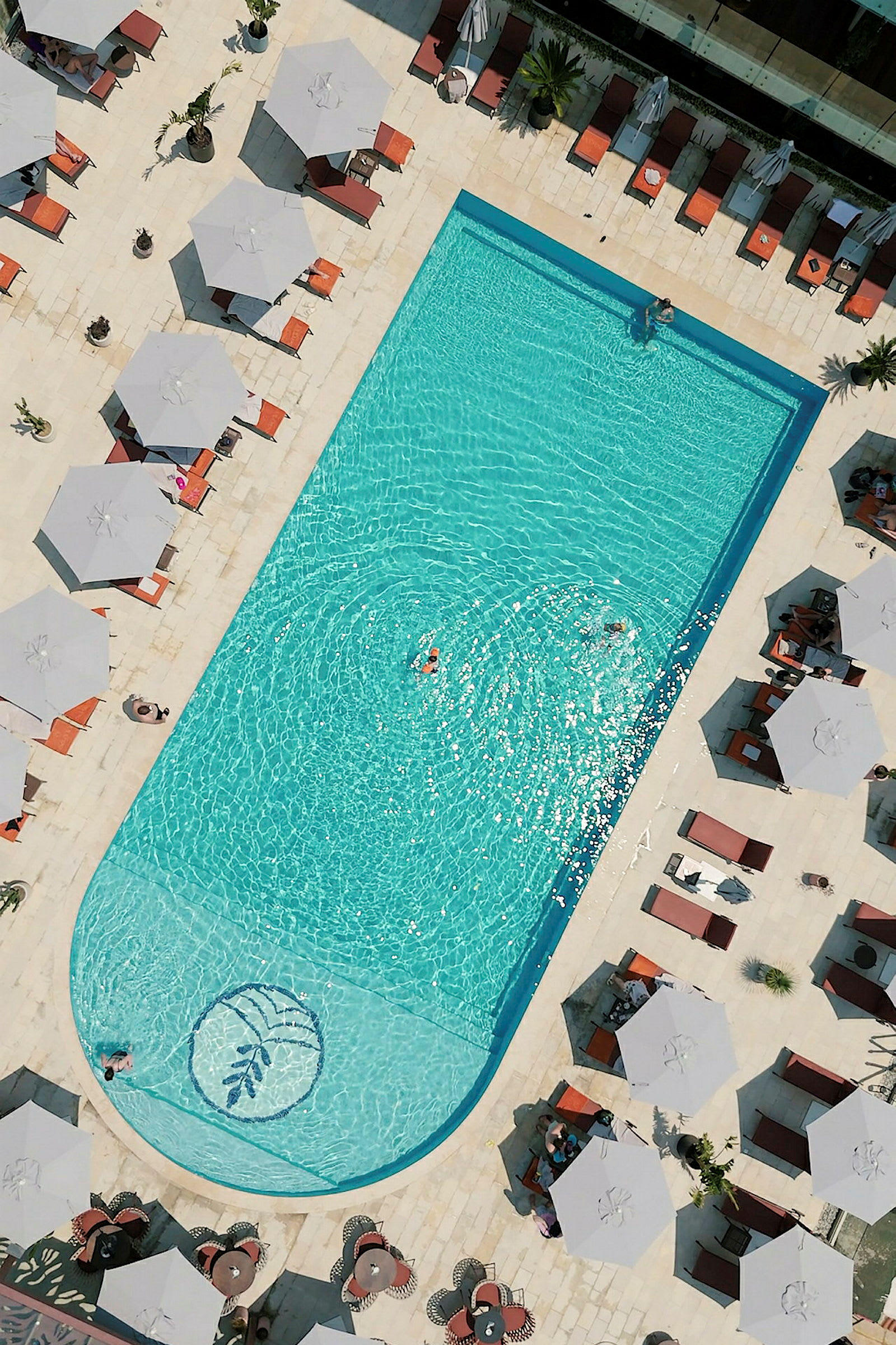 Vy uppifrån på en rektangulär pool omgiven av solstolar och parasoller. (AI-genererad text)