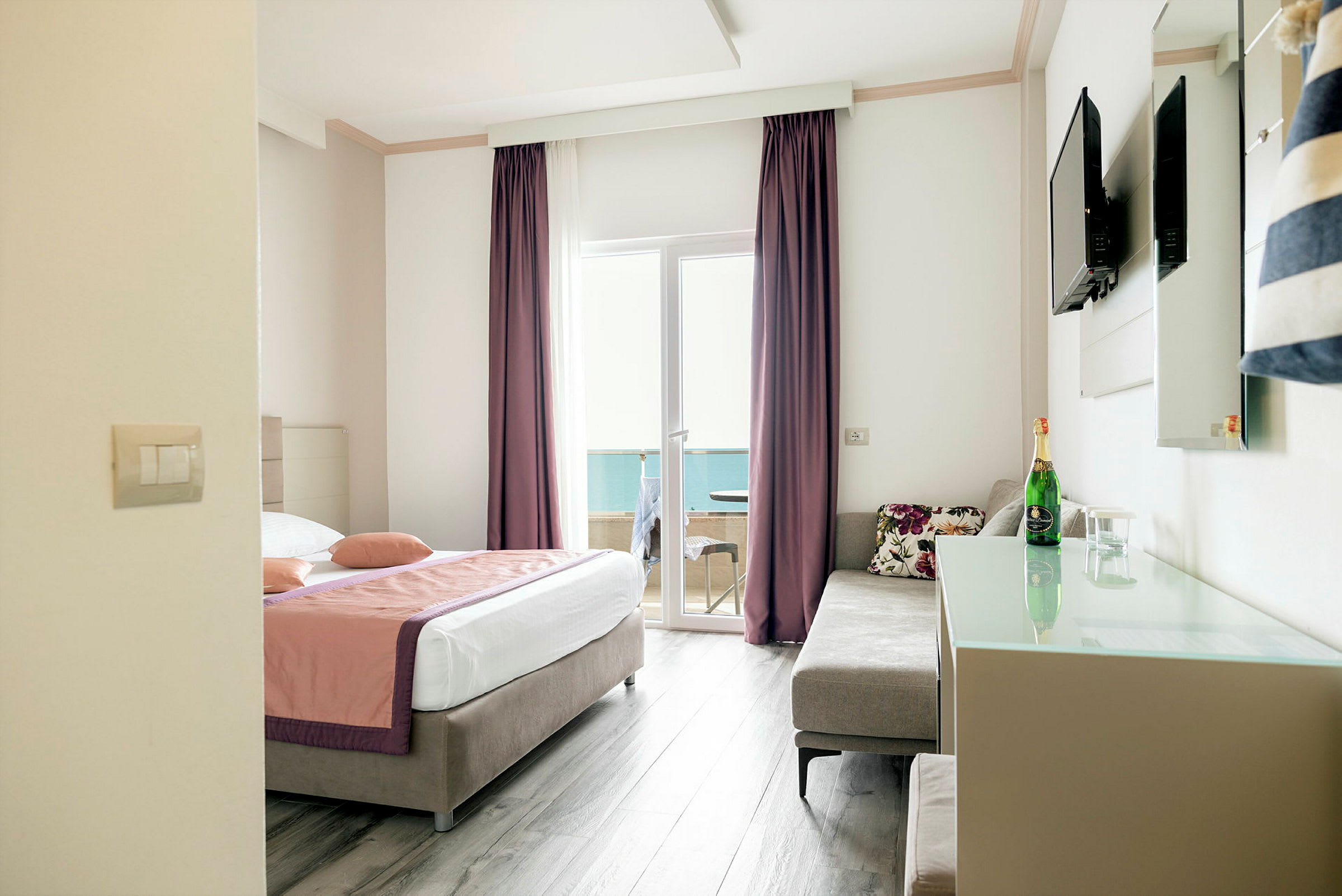 Hotelrum med en dubbelsäng, soffa, TV på väggen och glasdörr som leder till en balkong. (AI-genererad text)