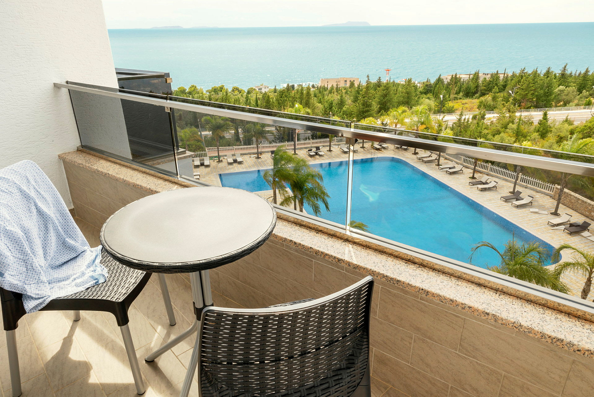 Vy från en balkong med bord och stolar som visar en pool och havet i bakgrunden. (AI-genererad text)