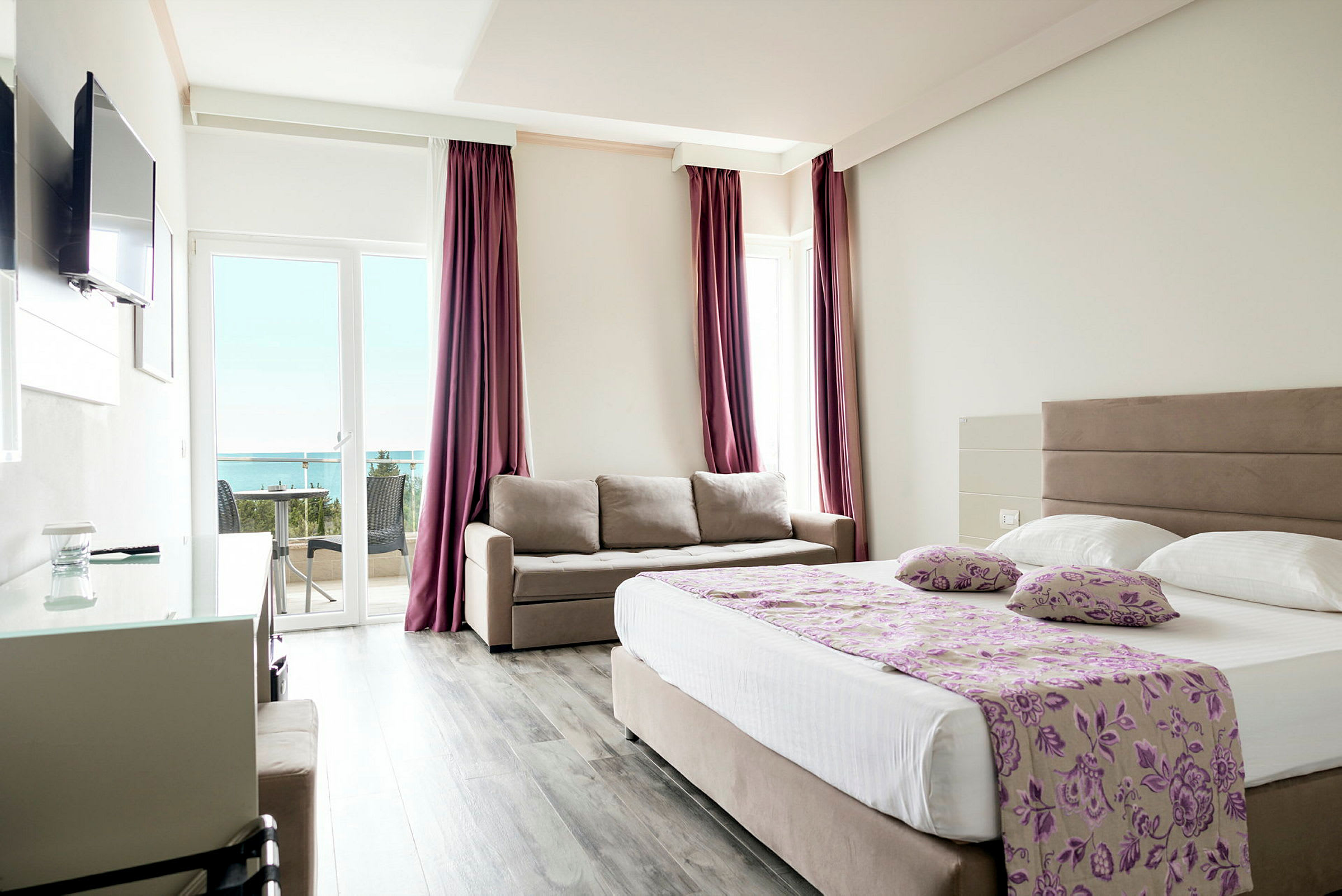 Ett hotellrum med en dubbelsäng, en soffa och en balkong med utsikt mot havet. (AI-genererad text)