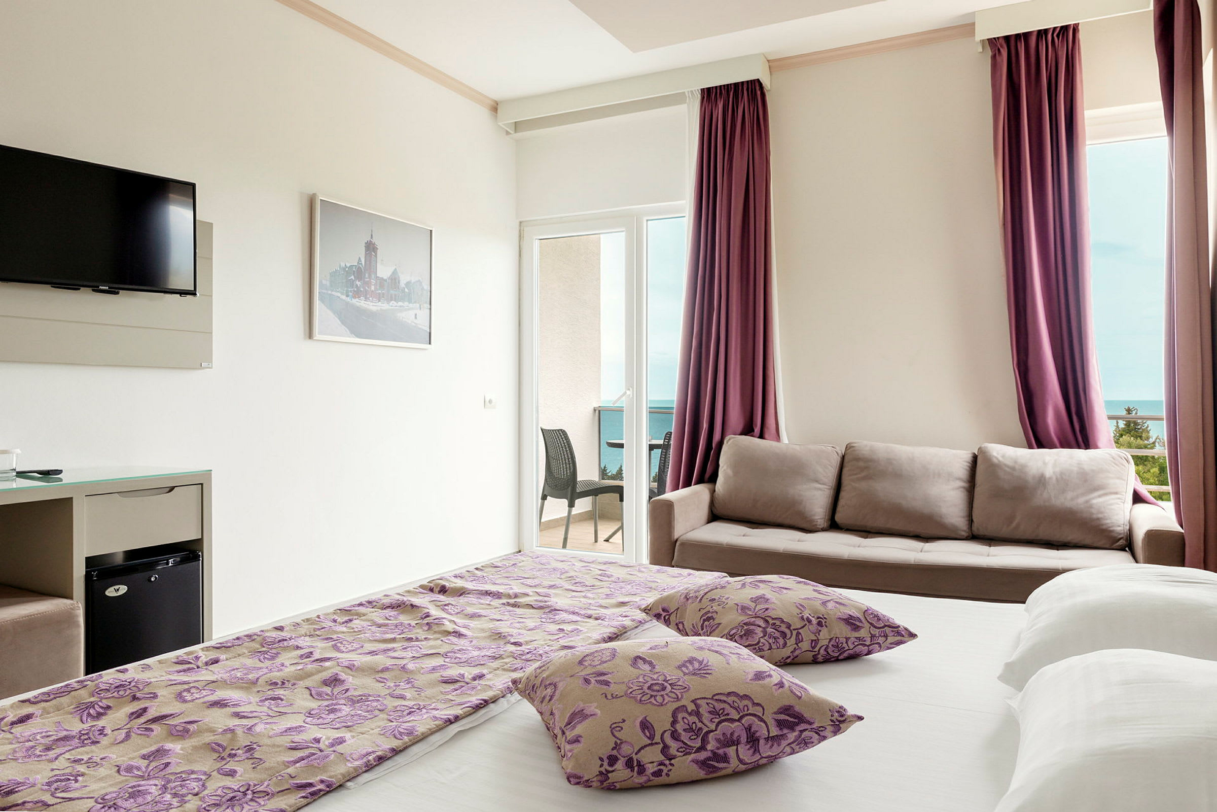 Hotellrum med säng, soffa, TV och en balkong med utsikt. (AI-genererad text)