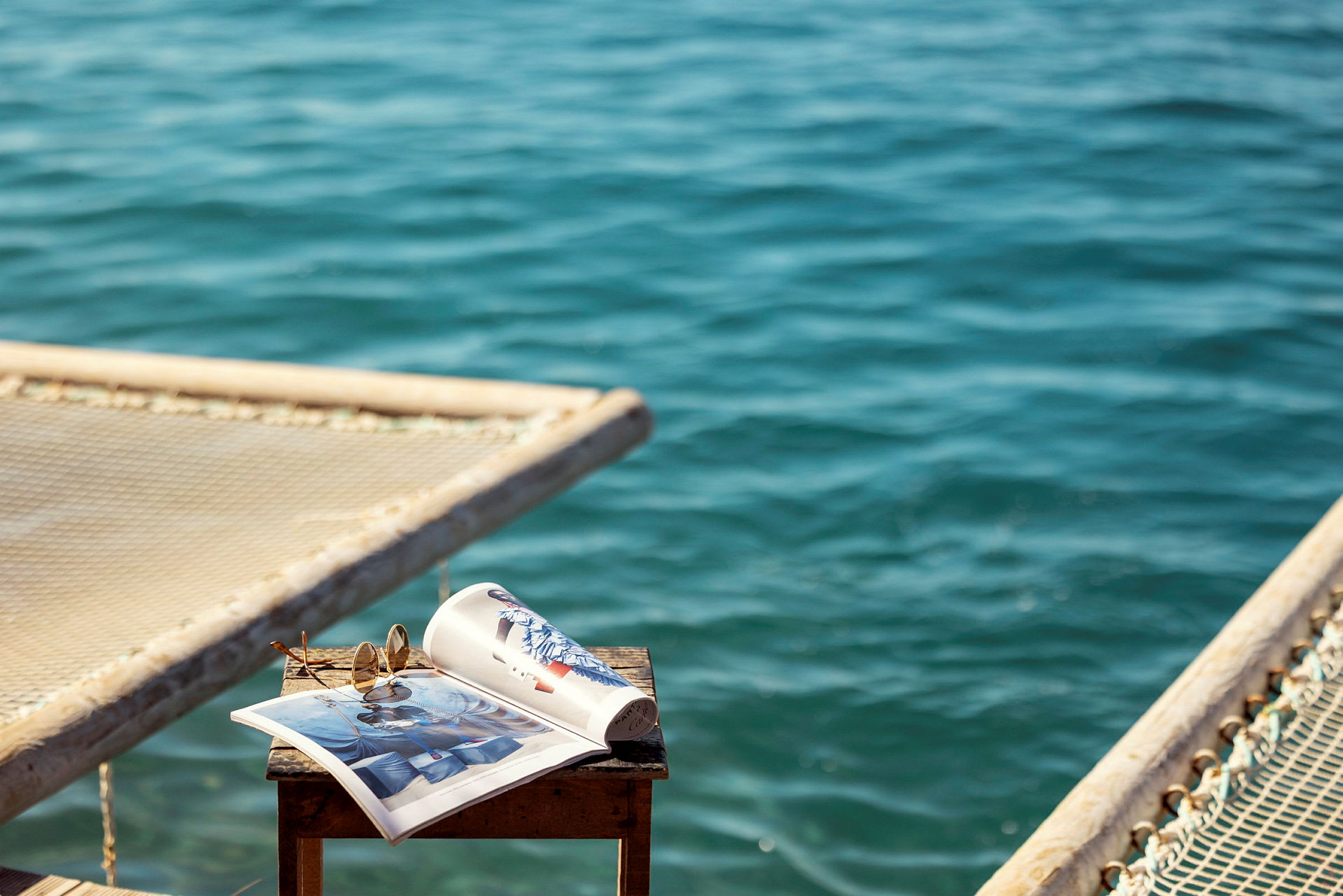 Ett bord med en öppen tidning och solglasögon, med havet i bakgrunden. (AI-genererad text)