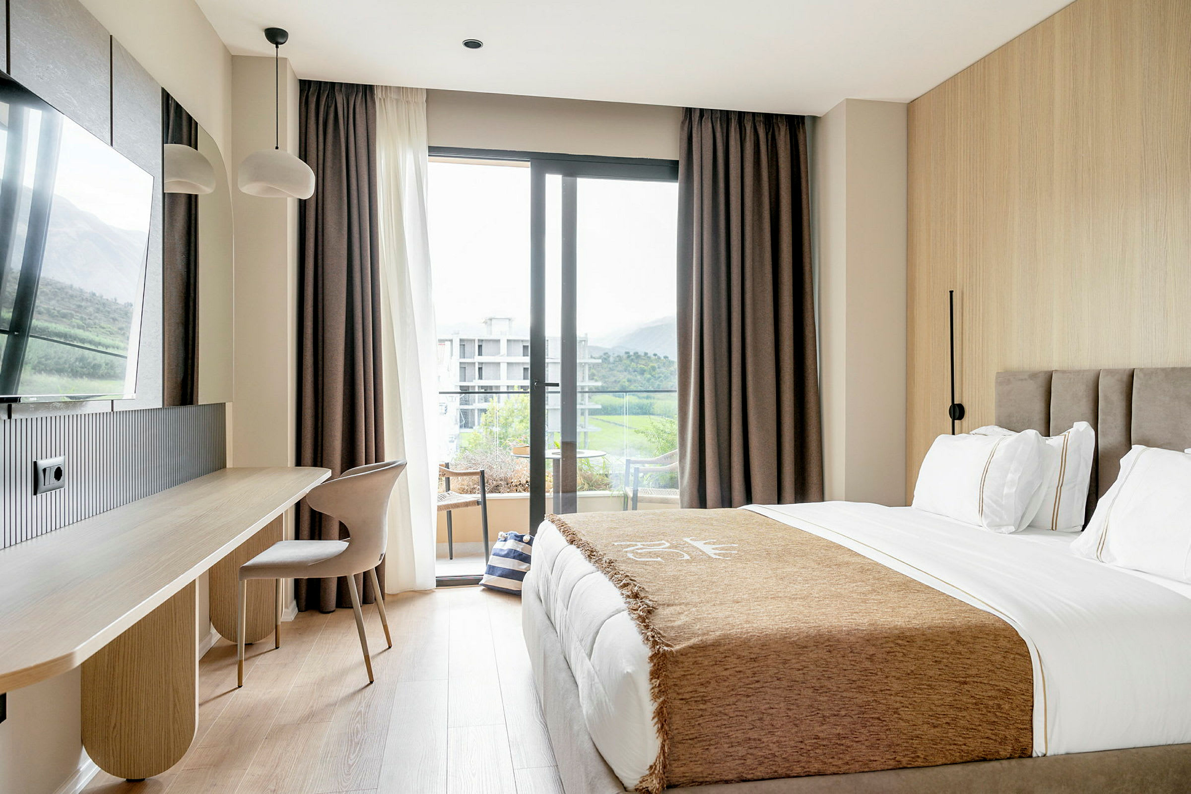 Ett hotellrum med en säng, skrivbord, stol och en balkongdörr med utsikt. (AI-genererad text)