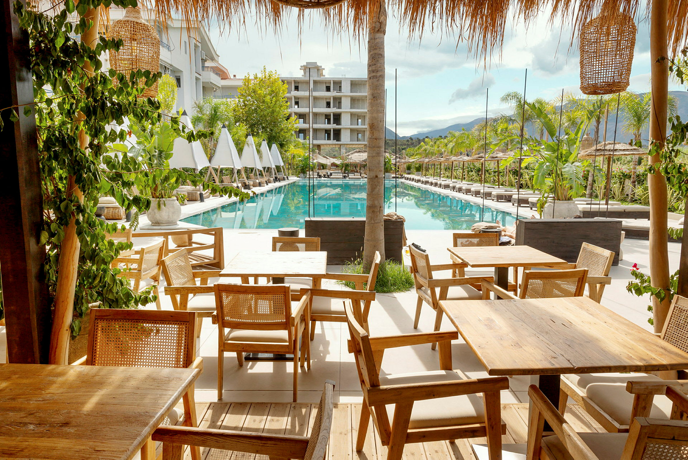 Bild av ett hotellområde med solstolar bredvid en rektangulär pool och träbord i förgrunden. (AI-genererad text)