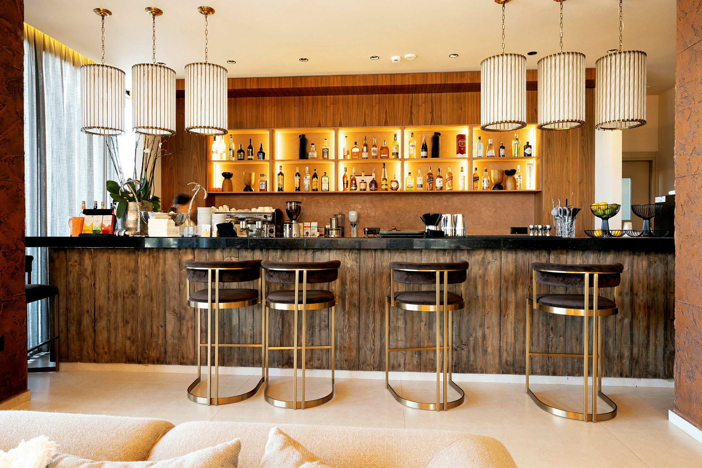 En elegant bar med fyra högstolar och hyllor fyllda med flaskor. (AI-genererad text)