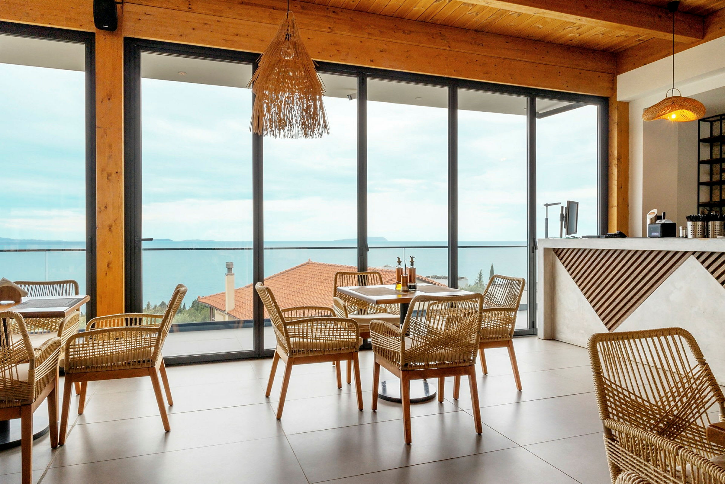 En restaurang med rottingmöbler och stora fönster som vetter ut mot havet. (AI-genererad text)