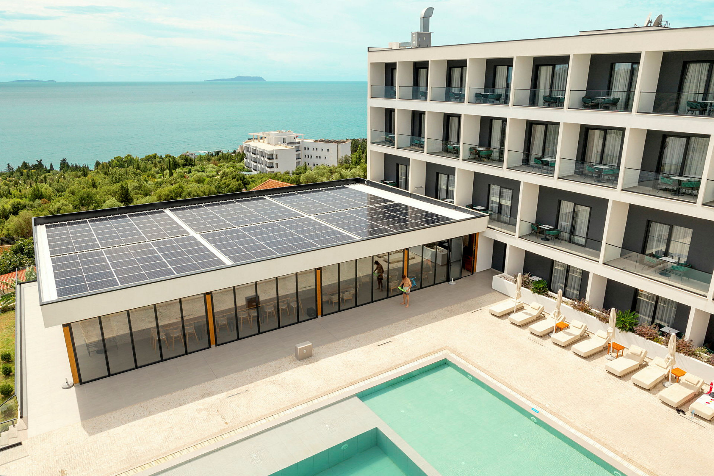 Hotellbyggnad med solpaneler, pool och solstolar, nära kusten. (AI-genererad text)