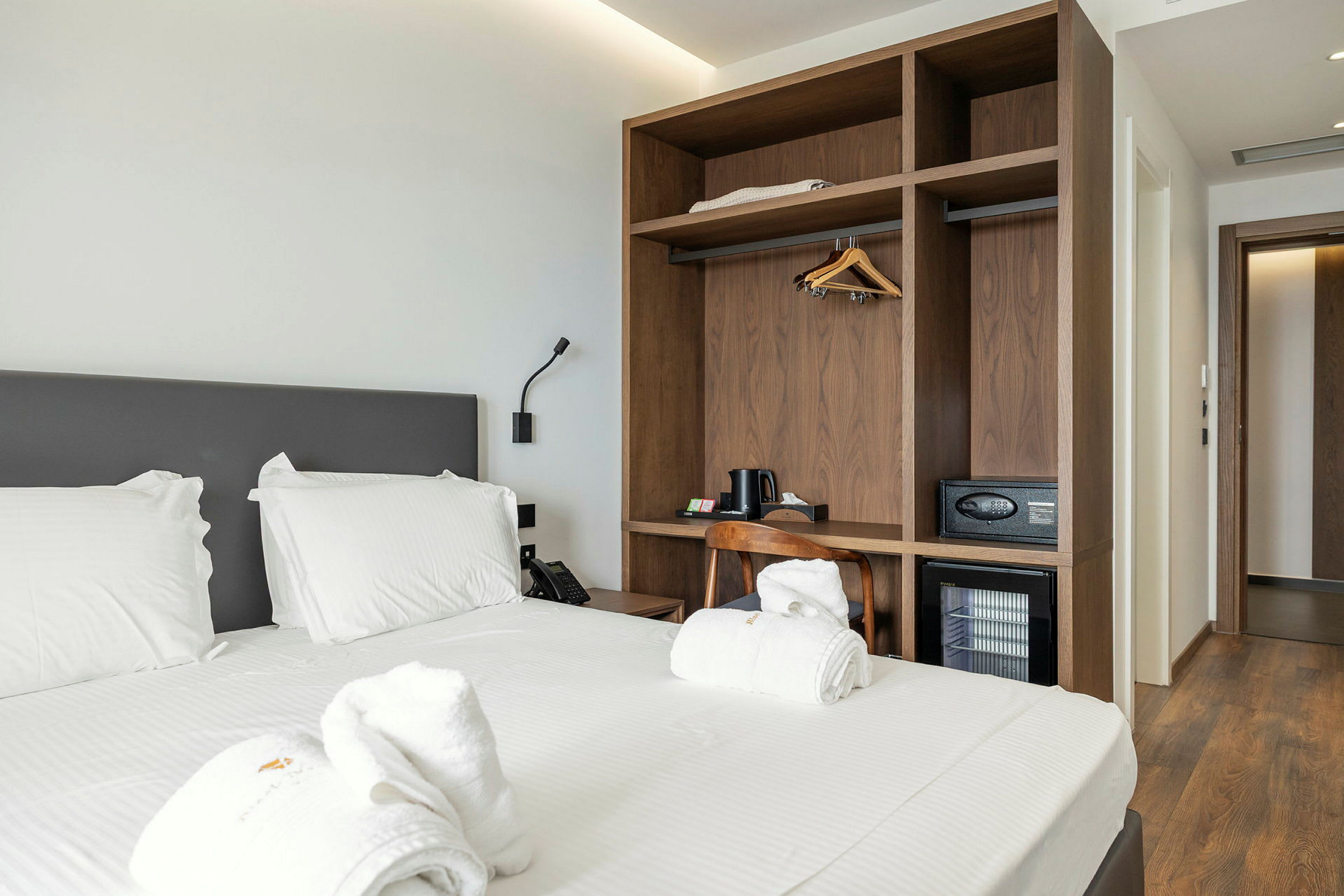 Hotellrum med en dubbelsäng, vit sängkläder, träskåp och dörrkarm i bakgrunden. (AI-genererad text)