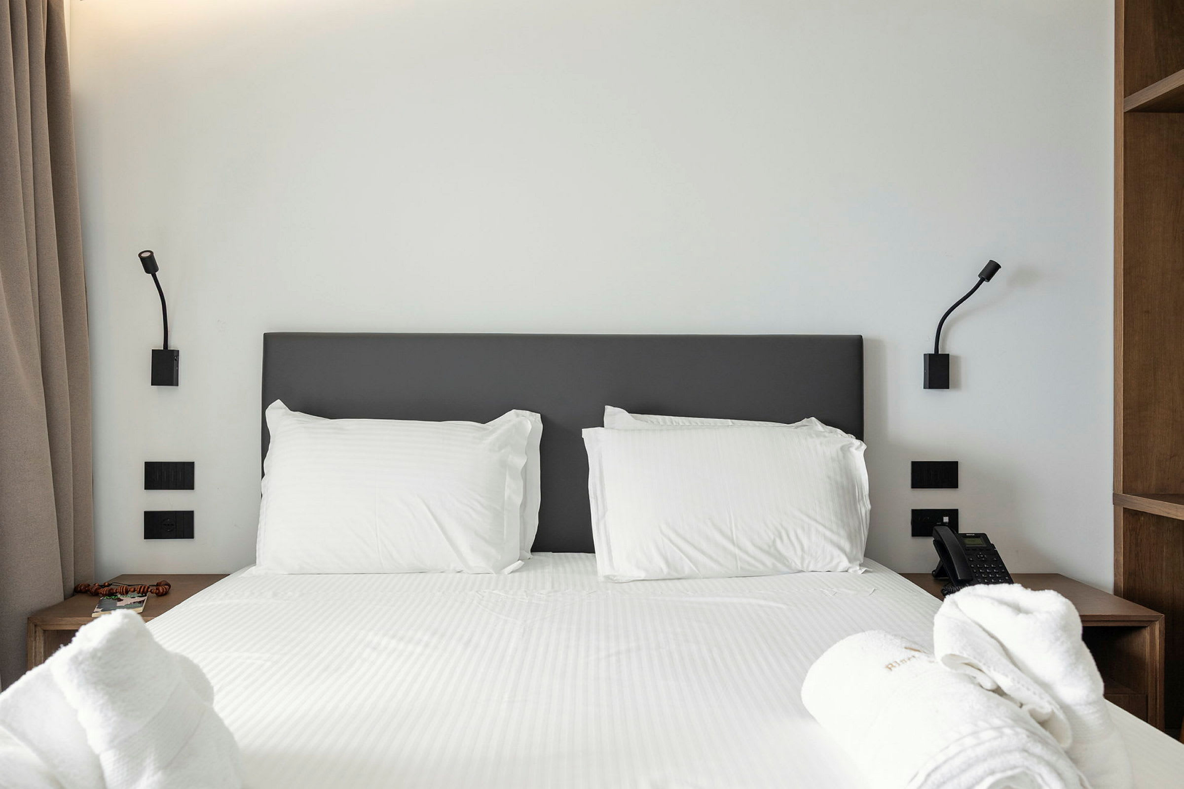 En hotellrumssäng med vita lakan och kuddar, flankerad av två nattlampor. (AI-genererad text)