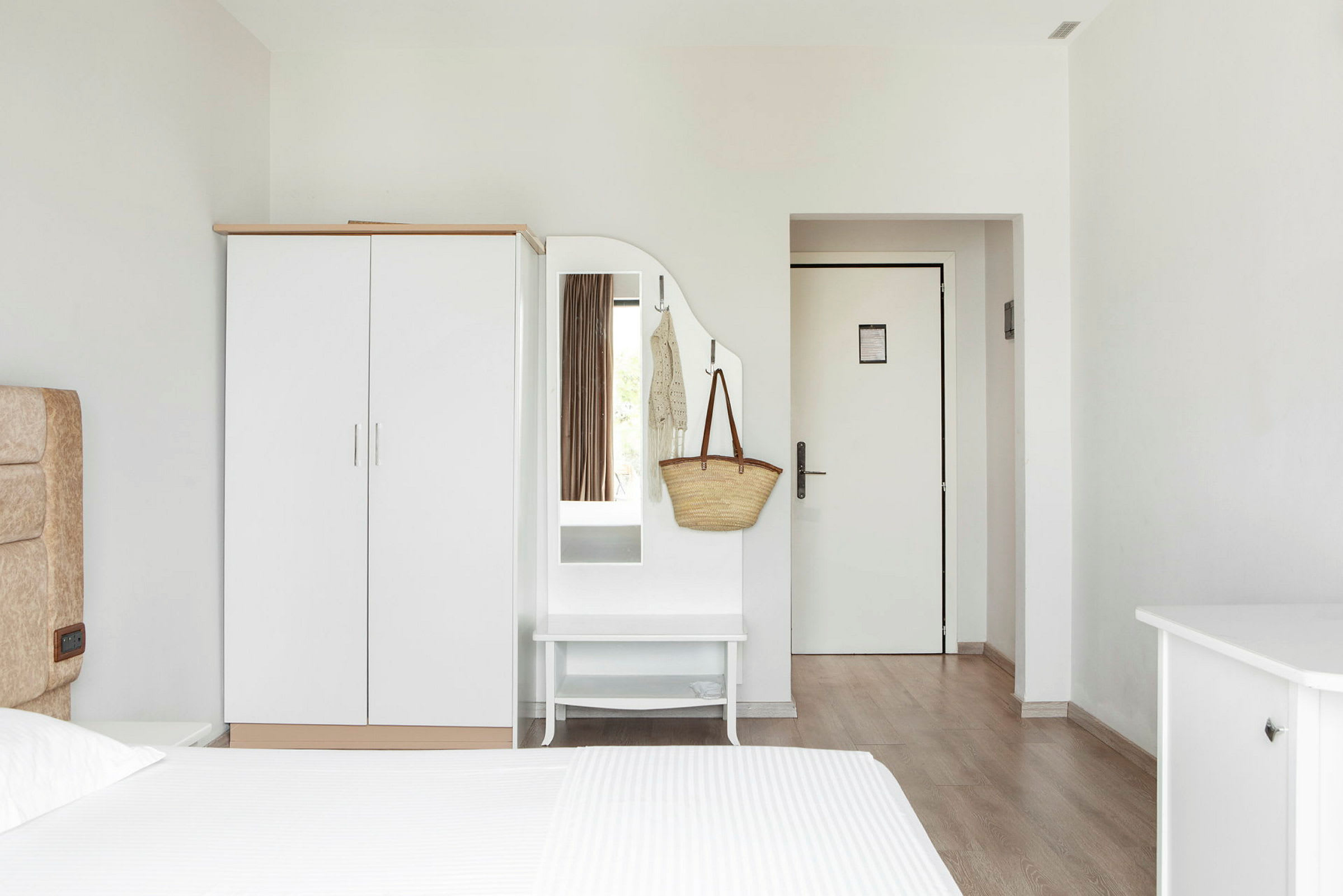 Ett hotellrum med en vit garderob, spegel och dörr. (AI-genererad text)