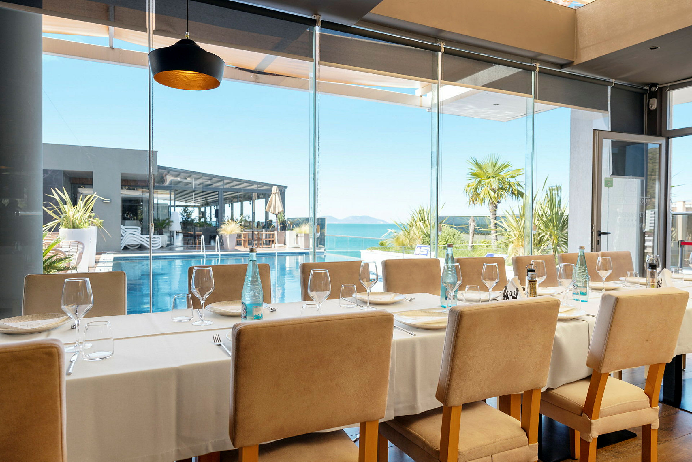 Restaurang med dukat bord och utsikt mot pool och hav. (AI-genererad text)