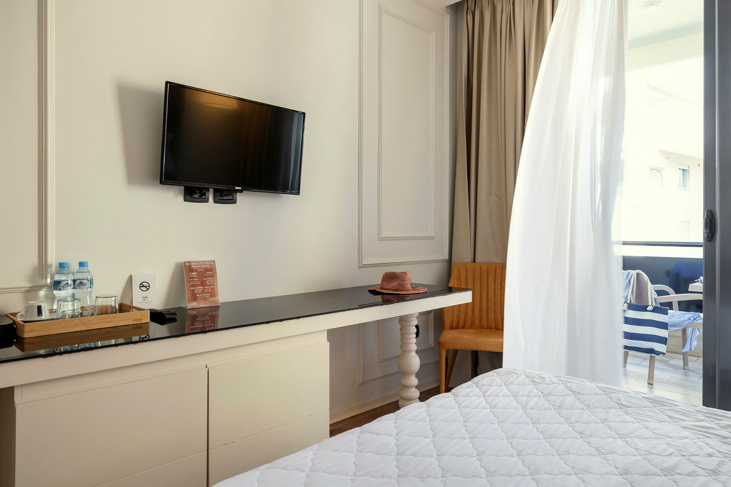 Hotellrum med TV på väggen, skrivbord, stol och delvis synlig balkong. (AI-genererad text)
