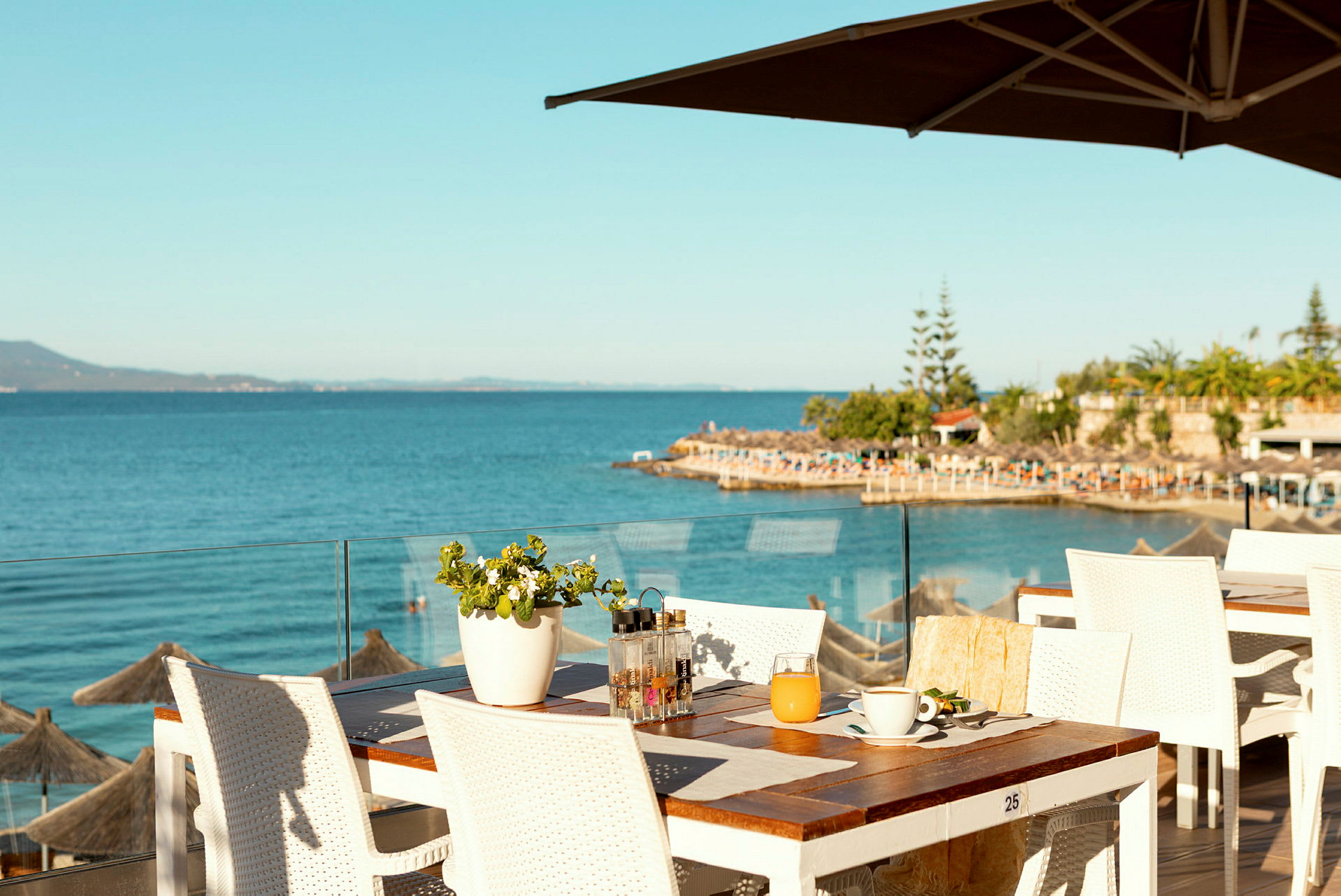 Utsikt över havet från en restaurangterrass med vita bord och stolar. (AI-genererad text)