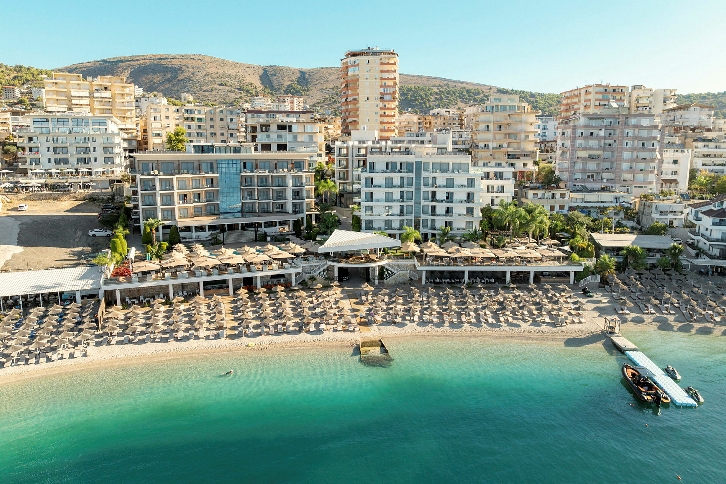 Vy över strand med solstolar och hotellbyggnader i bakgrunden. (AI-genererad text)
