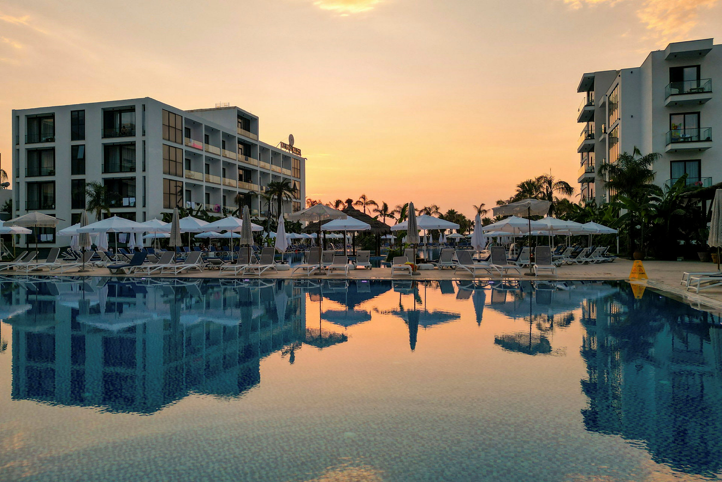 Hotellbyggnader och en pool vid solnedgång. (AI-genererad text)