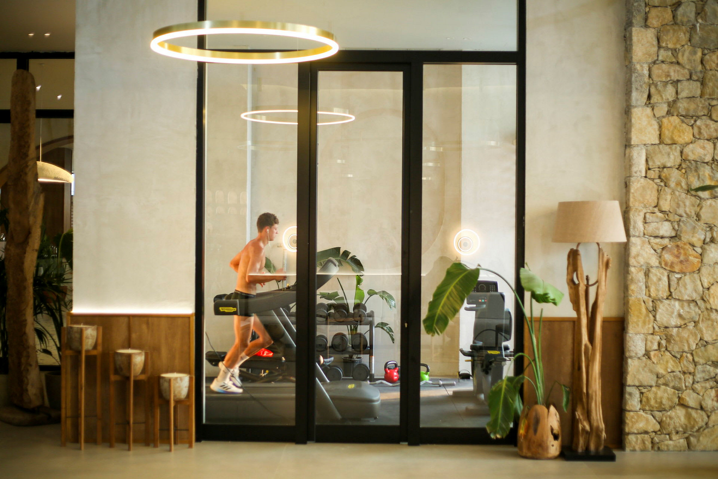 En person springer på ett löpband i ett modernt gym med växter och dekorativa trädetaljer. (AI-genererad text)