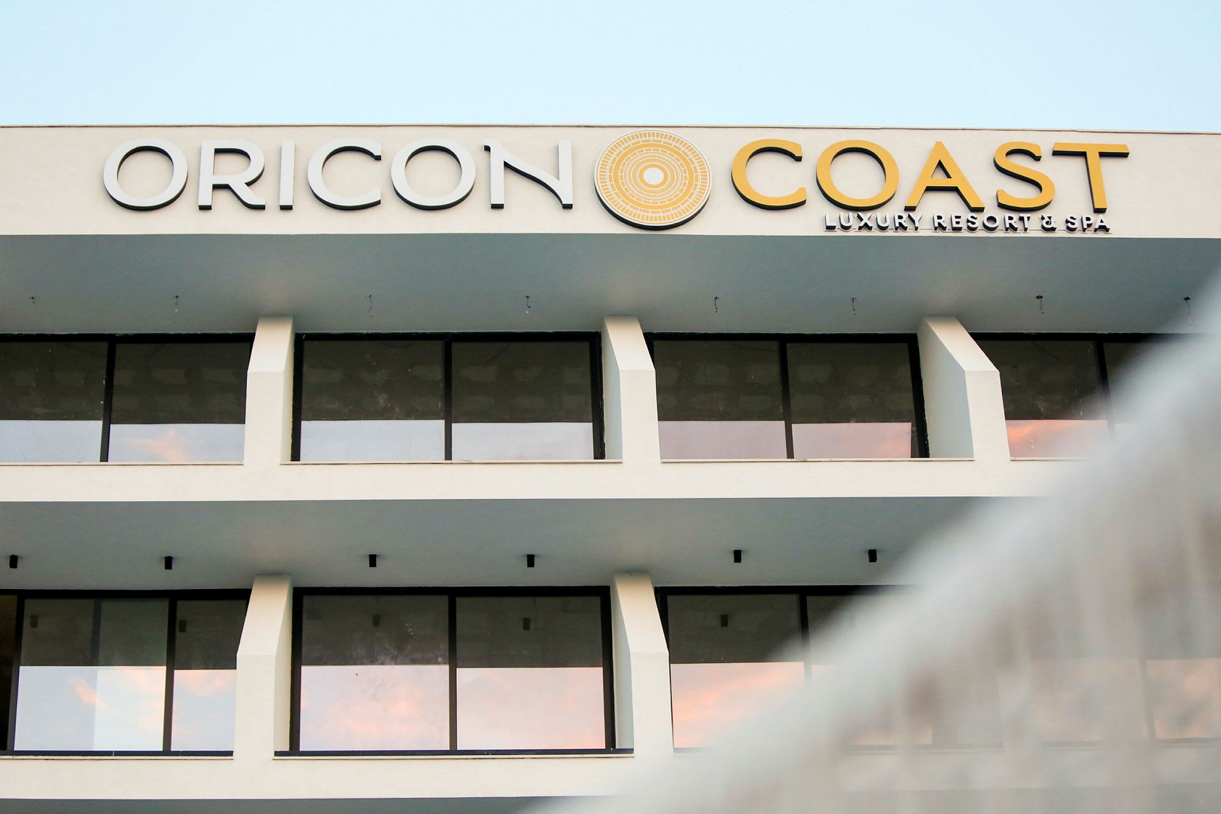Fasad av en hotellbyggnad med stora glasfönster och texten "Oricon Coast Luxury Resort & Spa" på toppen. (AI-genererad text)
