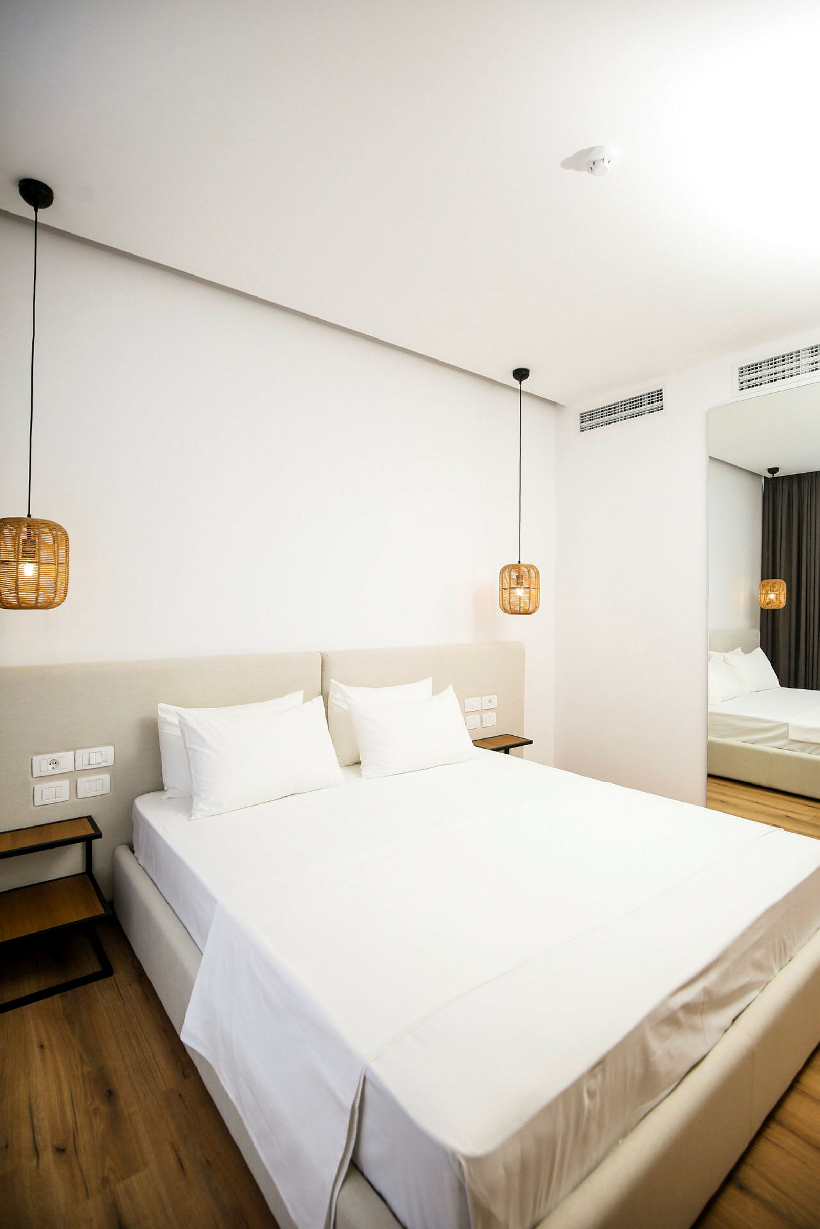 Ett modernt hotellrum med en stor säng bäddad med vita lakan. Hängande lampor i rotanstil flankerar sängen. (AI-genererad text)