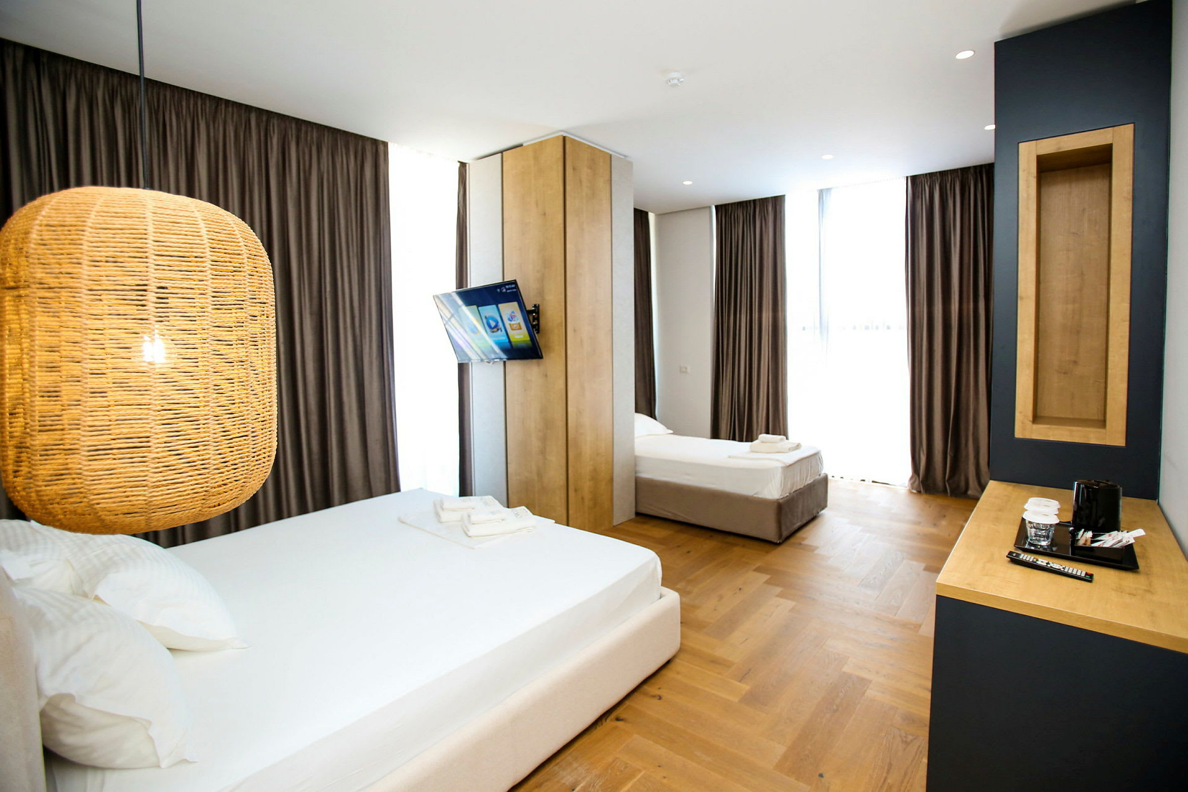 Ett hotellrum med två sängar, en hängande lampa, en väggmonterad TV och ett skrivbord med kaffekokare. (AI-genererad text)