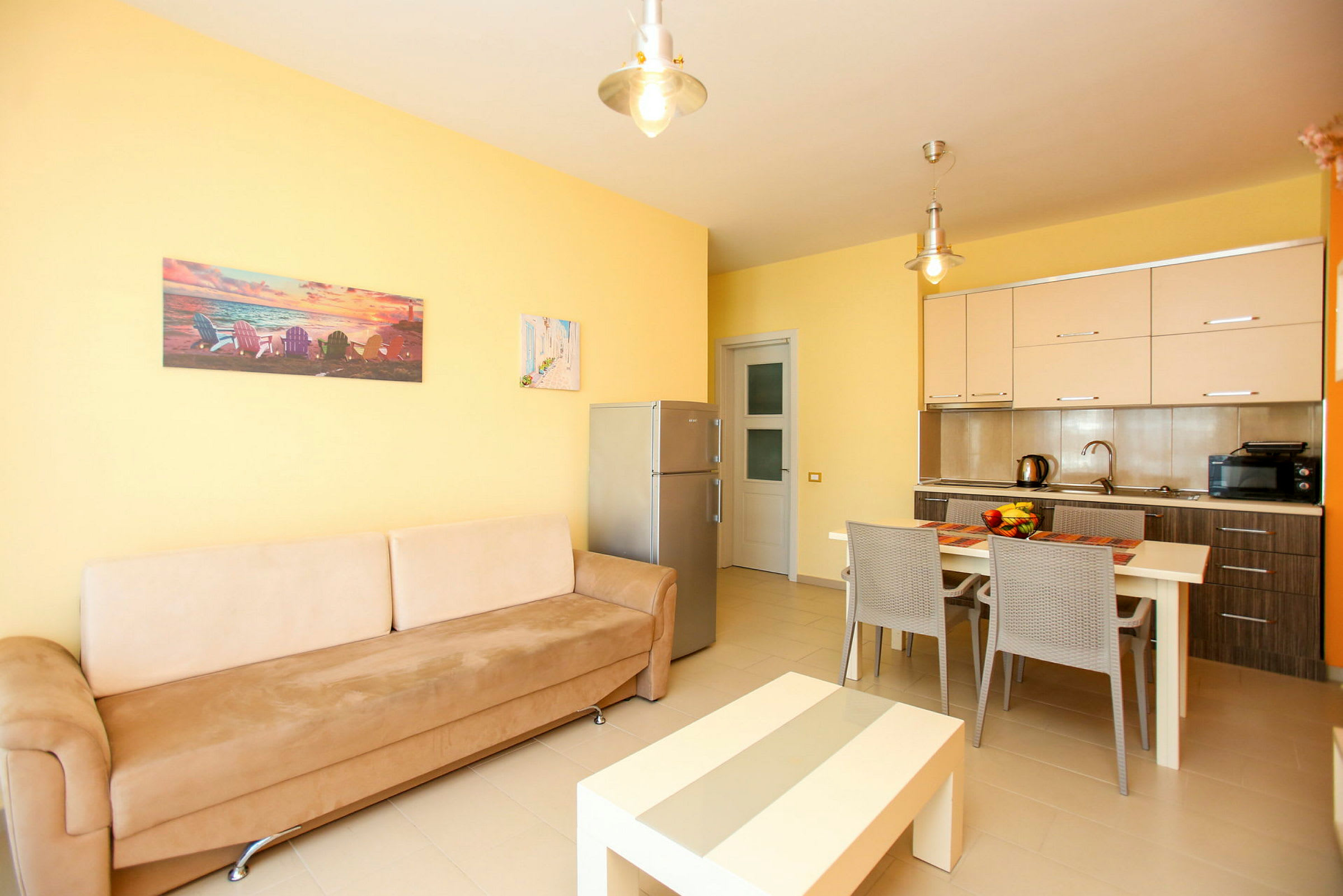 Ett vardagsrum och kök med beige väggar, en soffa, ett matbord och köksmöbler. (AI-genererad text)