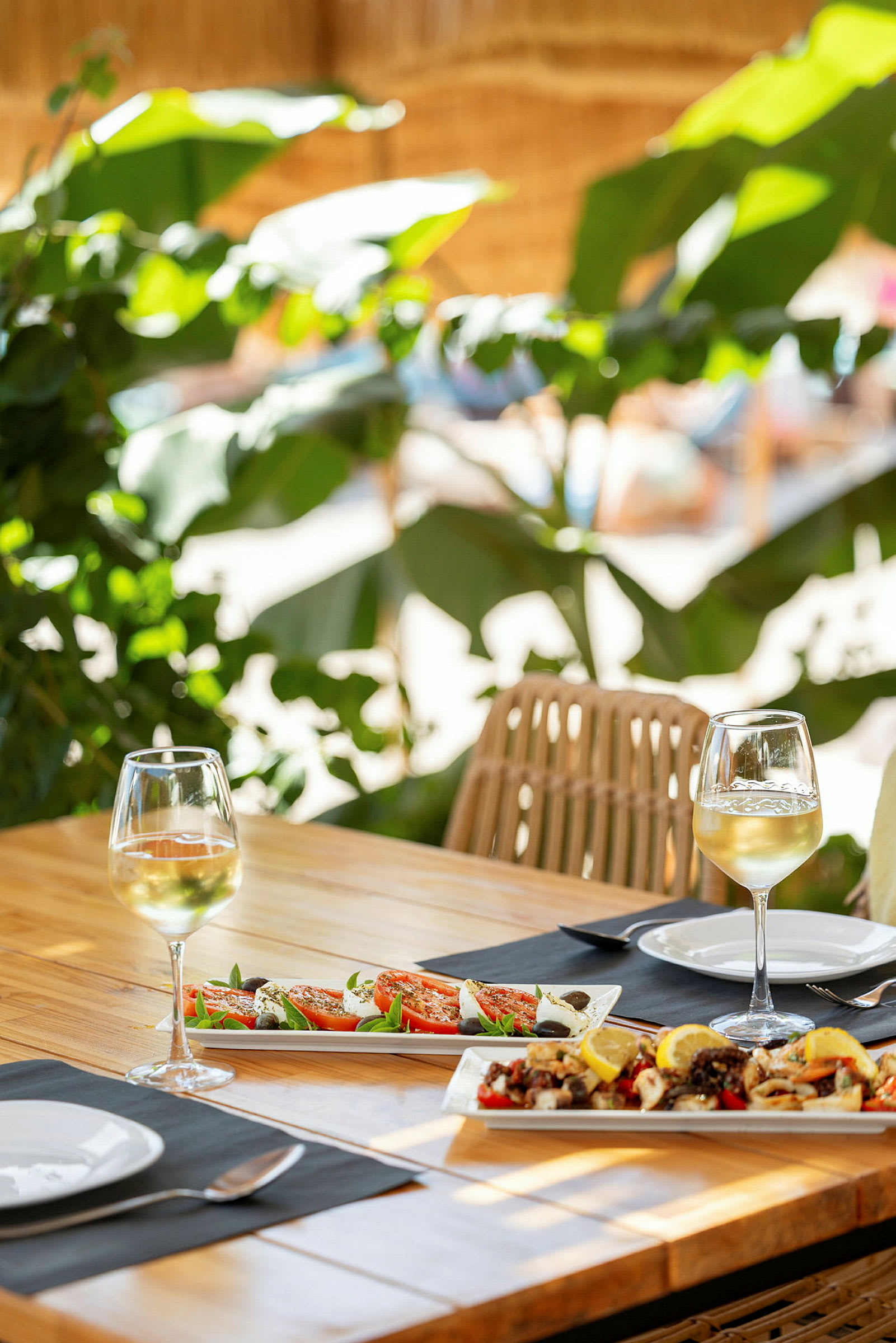 Två glas vitt vin på ett bord med maträtter och grönska i bakgrunden. (AI-genererad text)