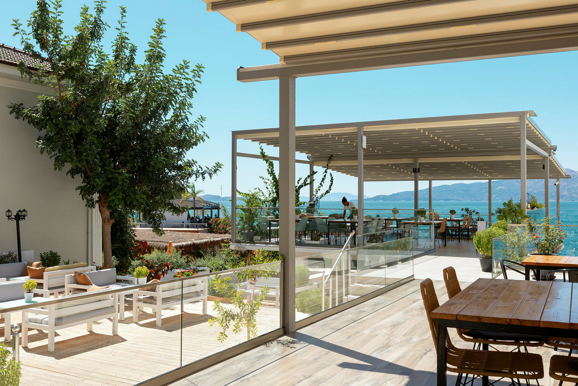 Bilden visar en utomhusservering med havsutsikt och bord under en pergola. (AI-genererad text)