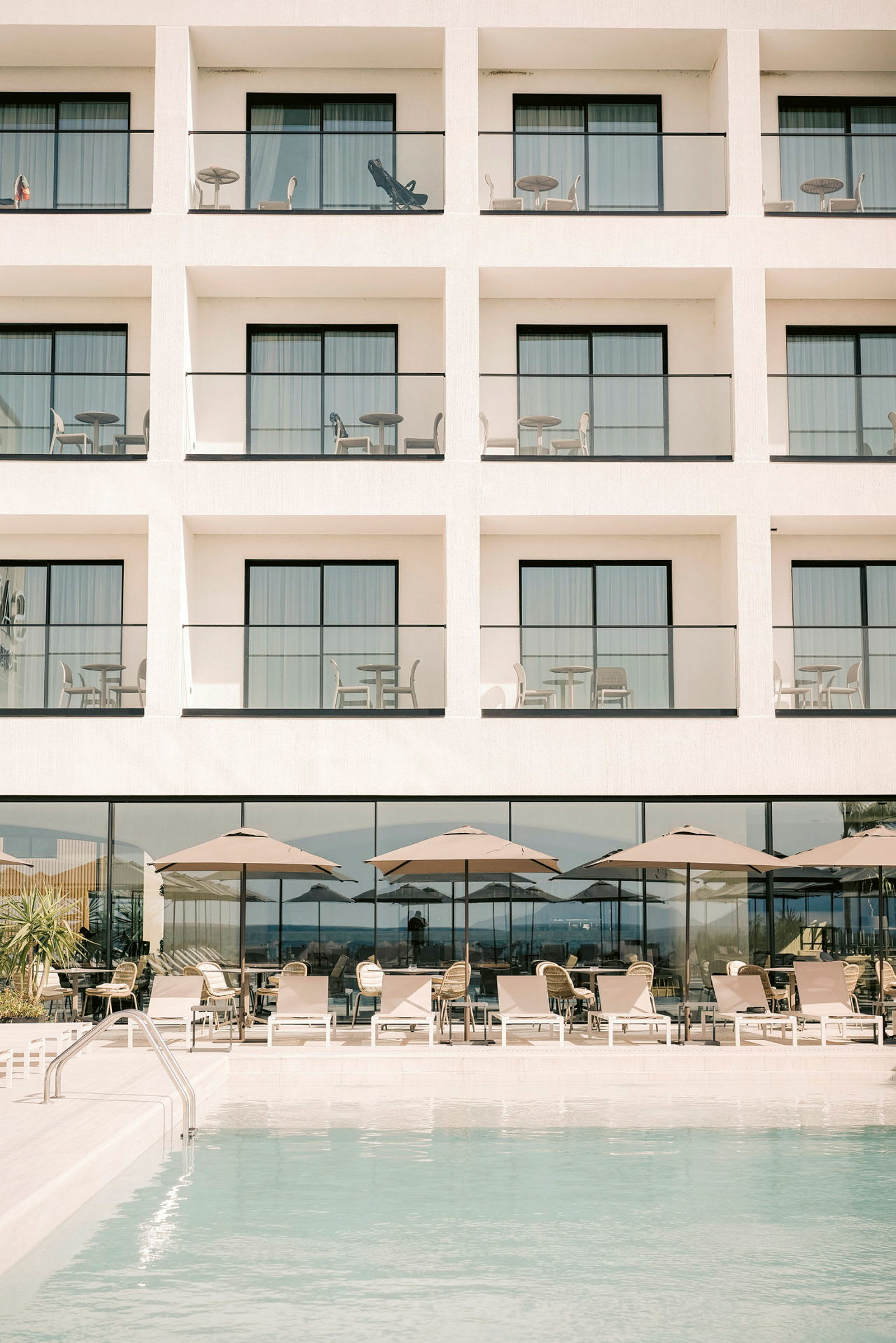 Hotellbyggnad med balkonger, nedanför finns en pool och sittplatser med parasoll. (AI-genererad text)