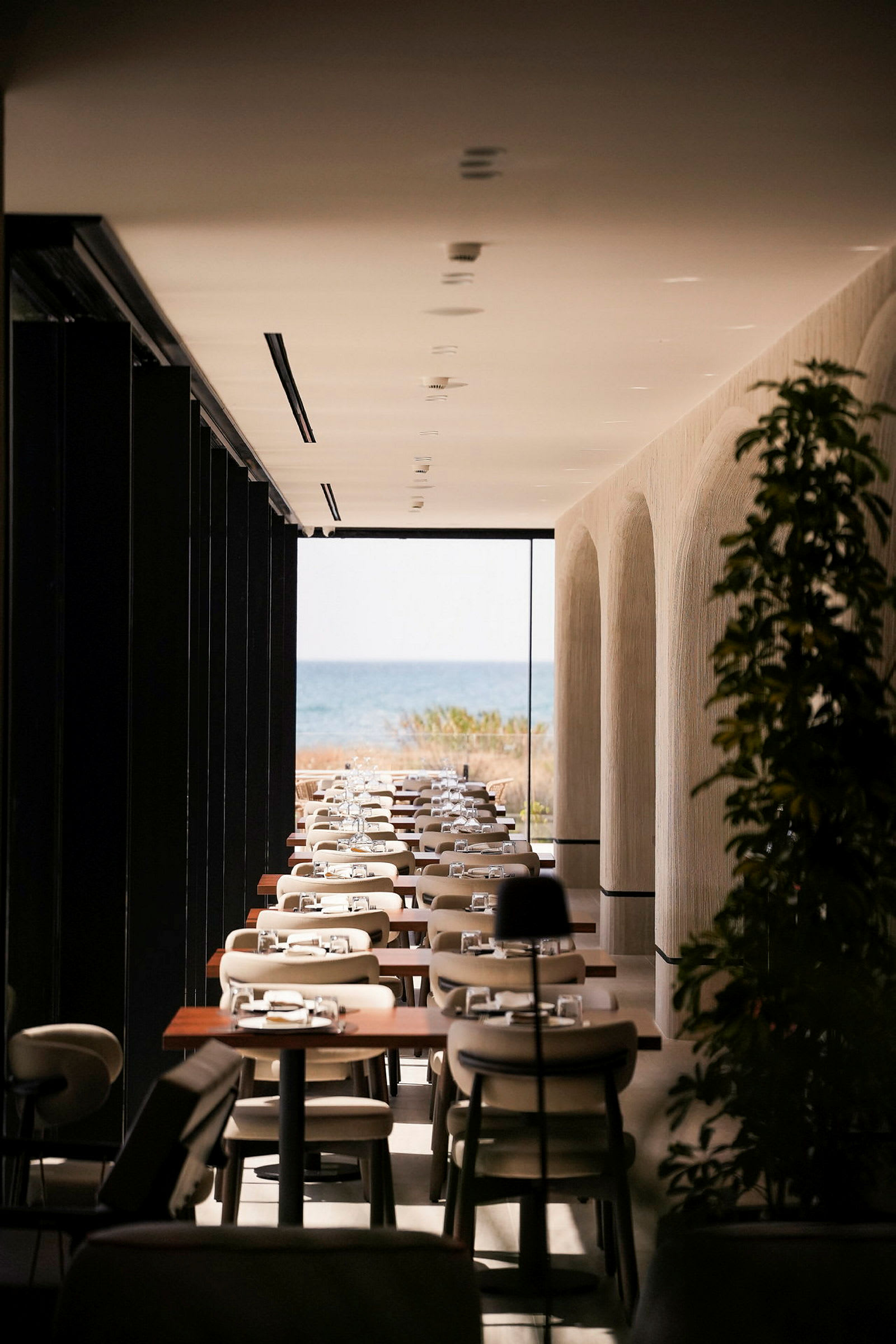 Ett modernt inrett restaurangutrymme med dukade bord och en vy över havet i bakgrunden. (AI-genererad text)