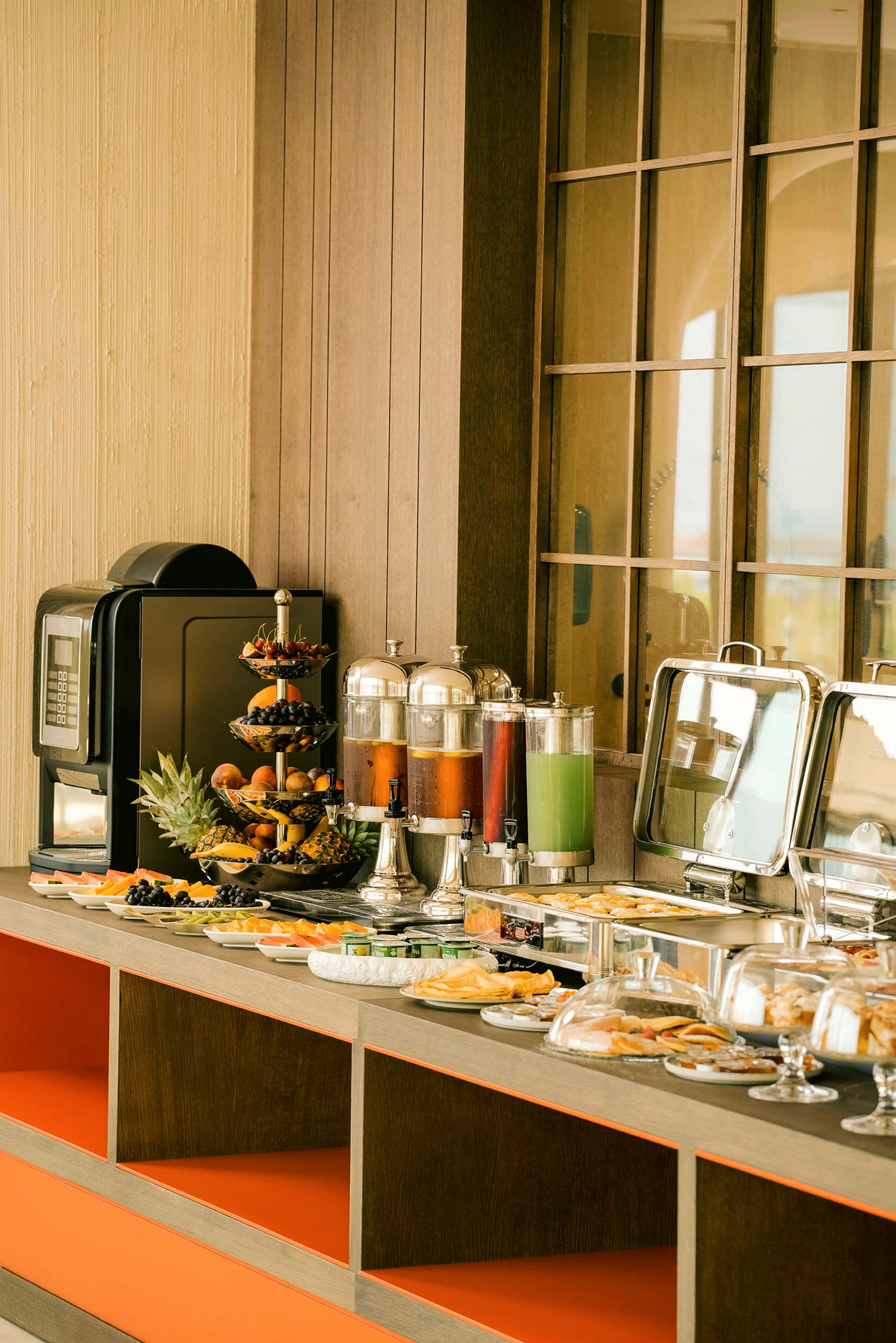 Ett frukostbuffébord med olika maträtter, frukter, juiceautomater och en kaffemaskin. (AI-genererad text)