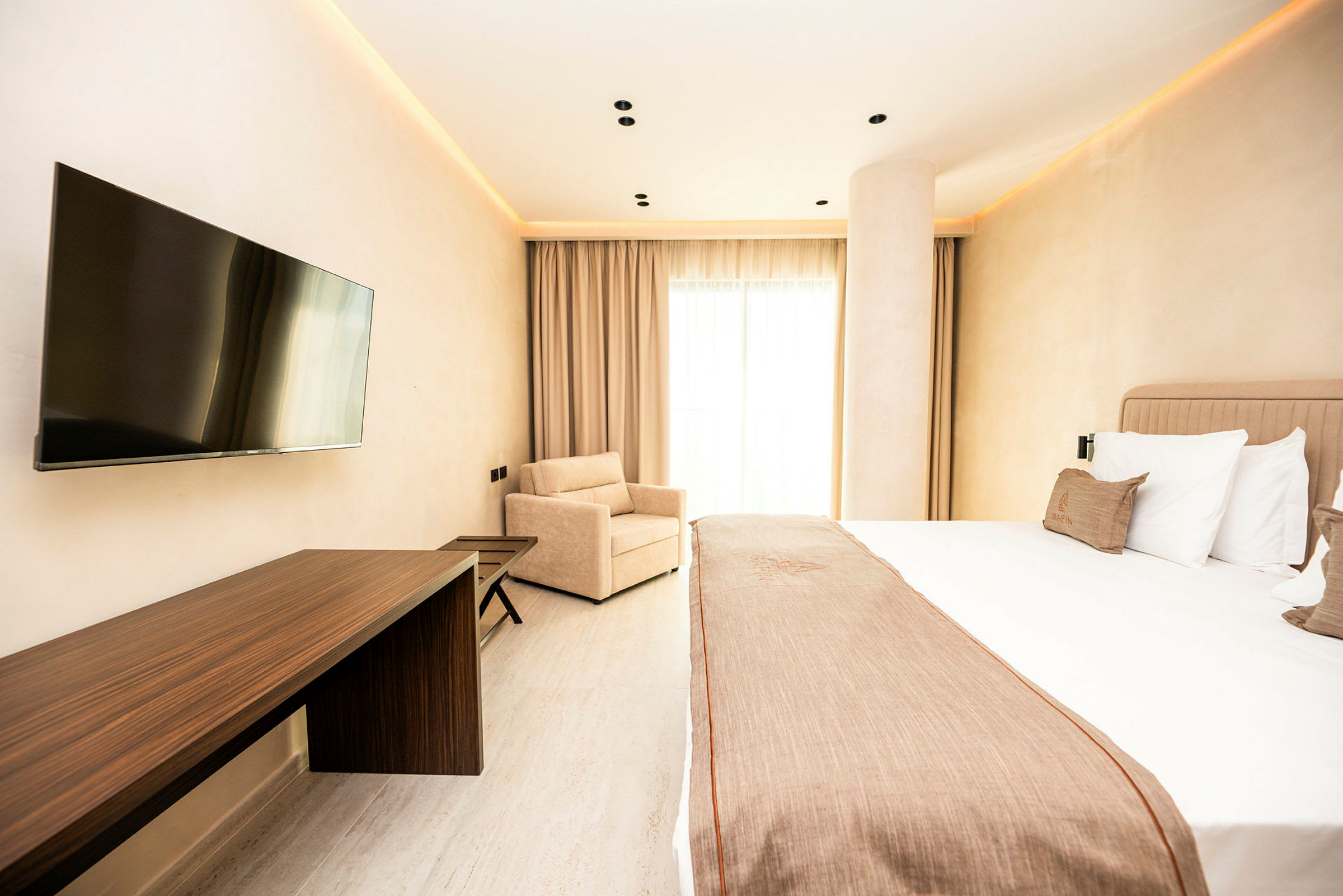 Ett hotellrum med en stor säng, en platt-TV på väggen, skrivbord och fåtölj. (AI-genererad text)