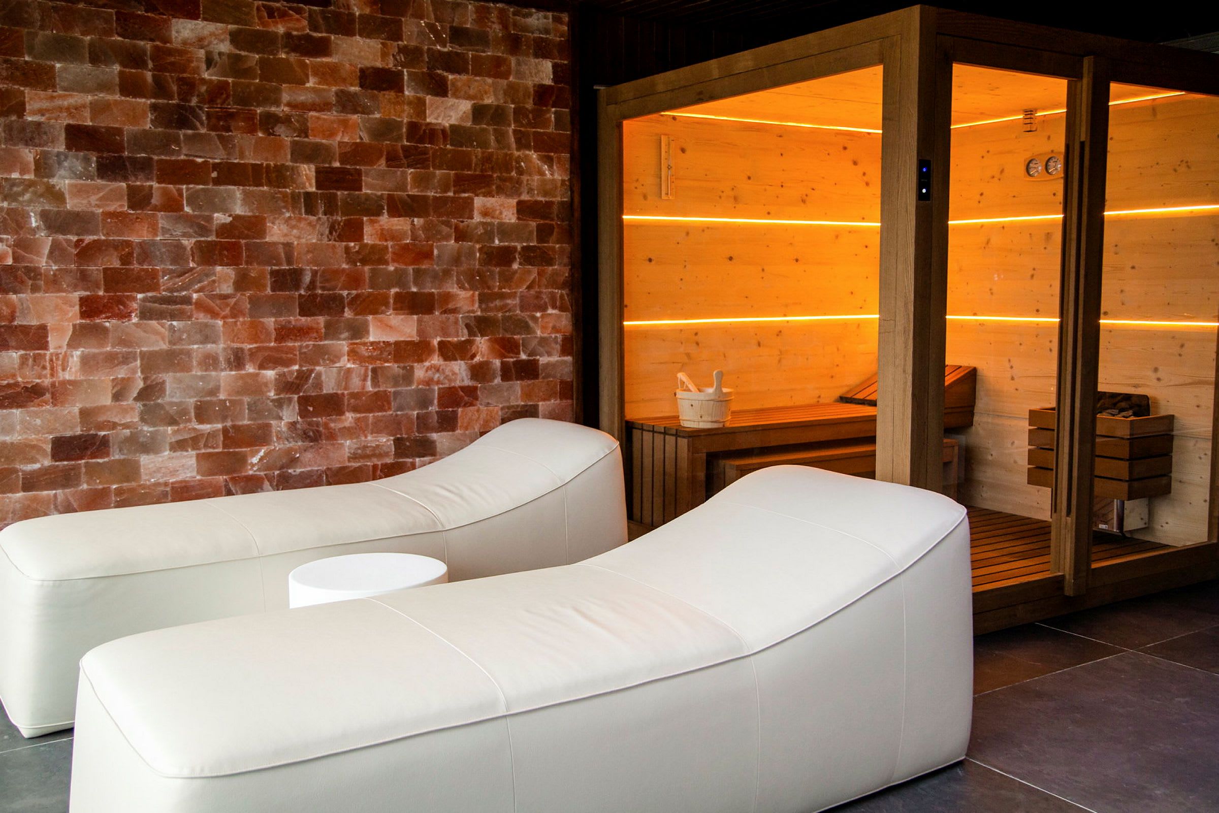 Relaxutrymme med två vita liggstolar och en bastu med träpanel belyst med orange-ljus. (AI-genererad text)