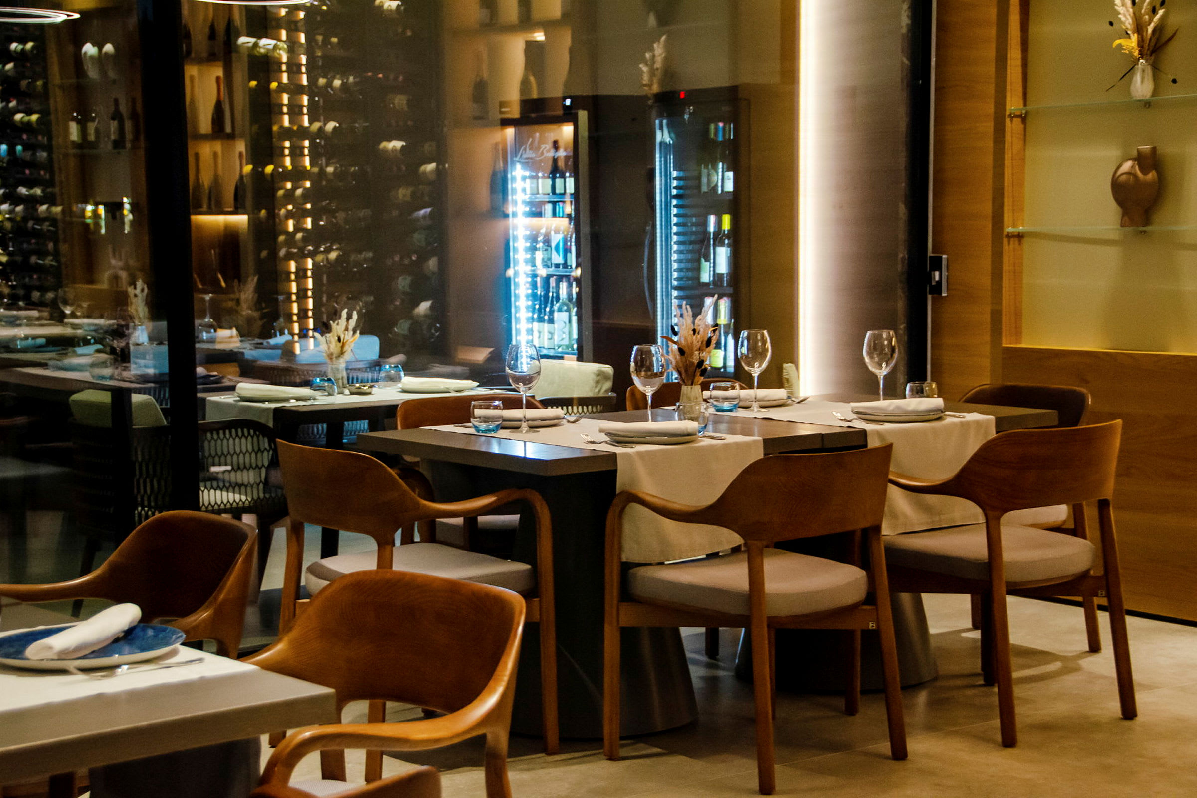 En elegant och modern restaurang med uppdukade bord och vinförvaring i bakgrunden. (AI-genererad text)