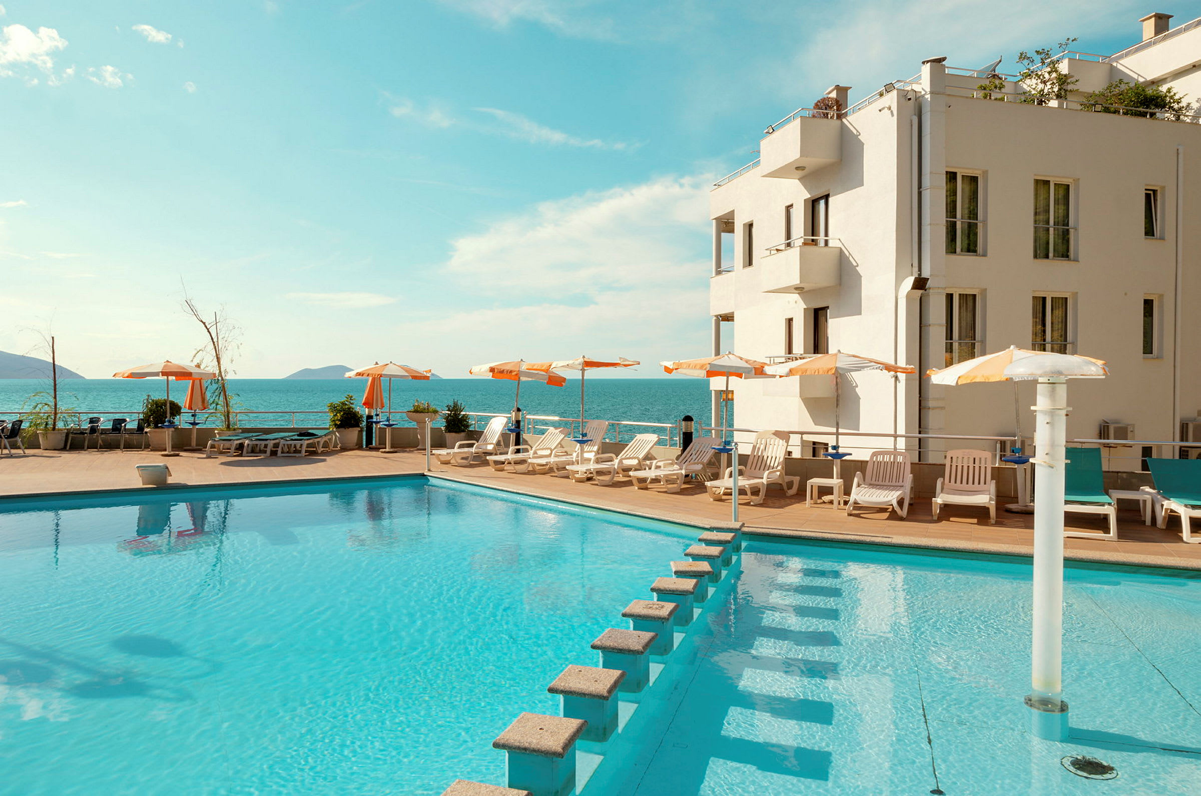 En pool med solstolar och parasoller vid ett hotell, med havsutsikt. (AI-genererad text)