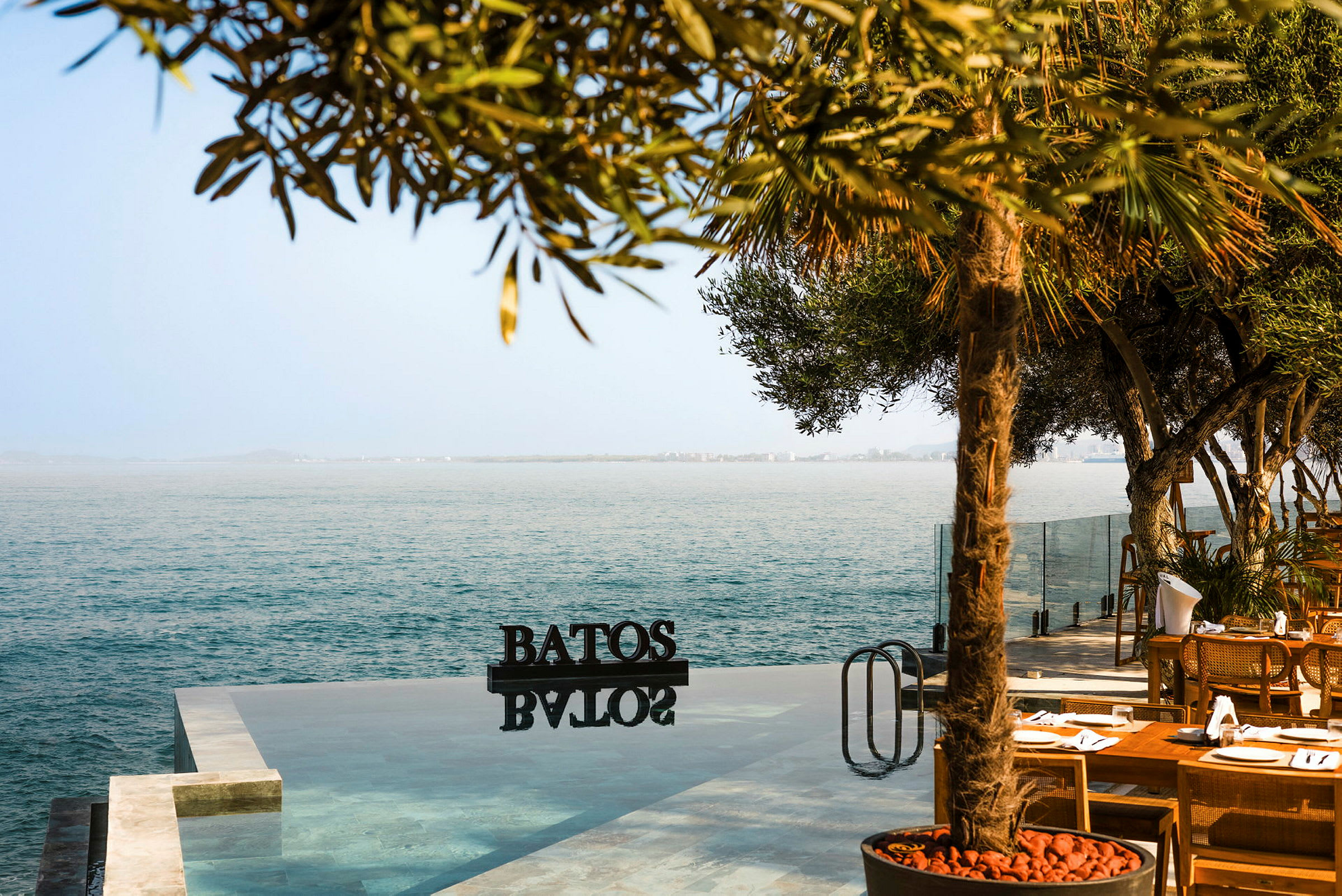 En infinitypool som vetter mot havet med träd och sittområde i förgrunden. (AI-genererad text)
