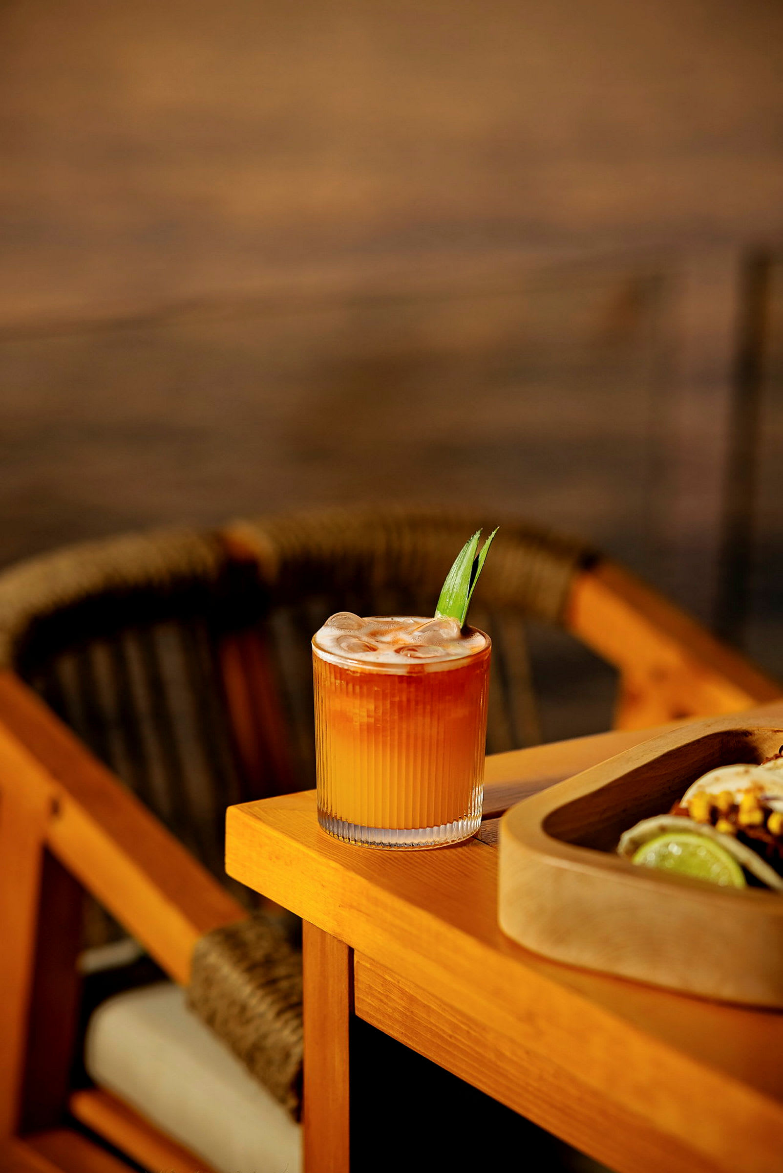 Ett glas med en orange drink toppad med is och dekorerad med ett blad står på ett träbord. (AI-genererad text)