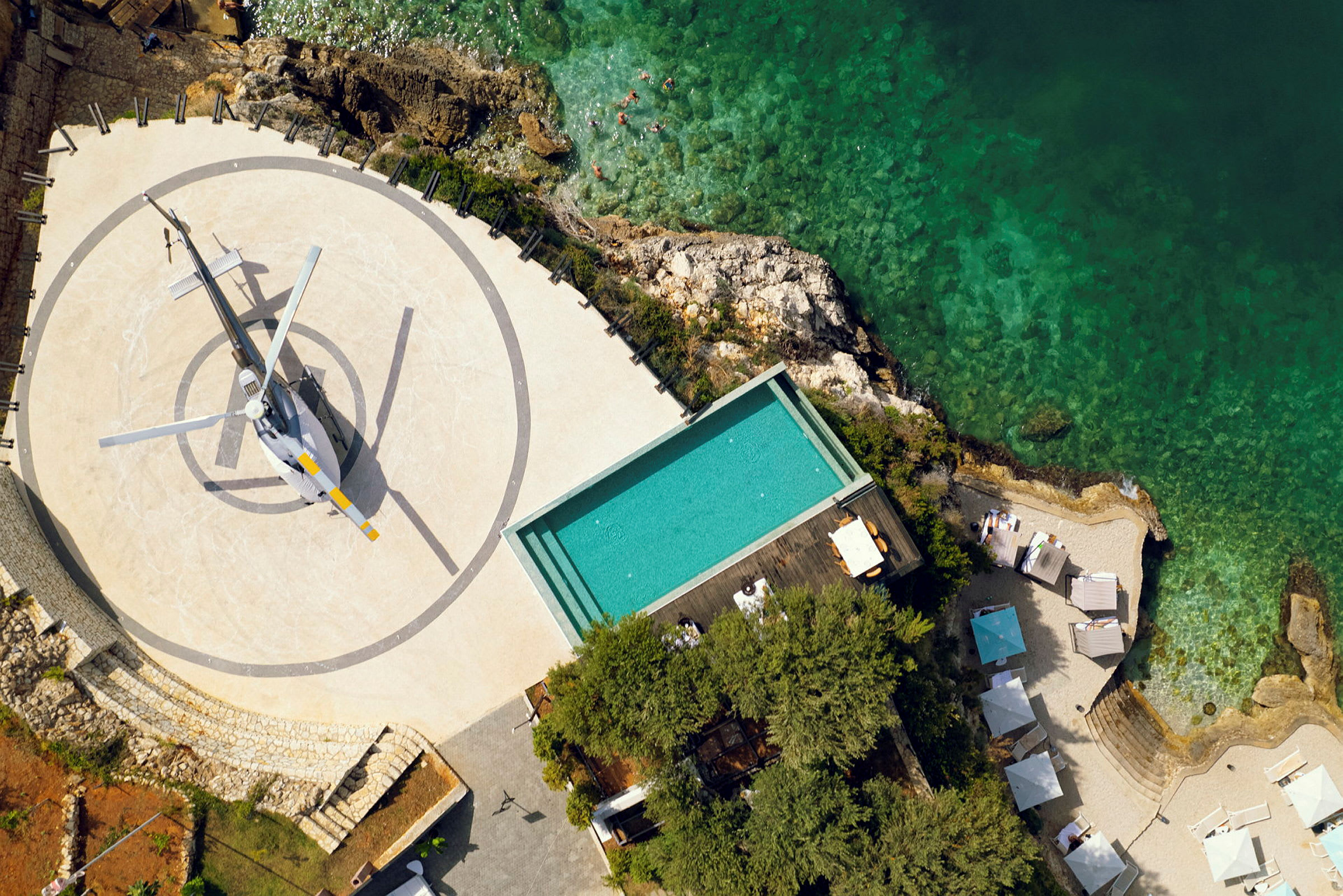 Flygbild av en helikopter på en landningsplattform nära en pool och kustlinje. (AI-genererad text)