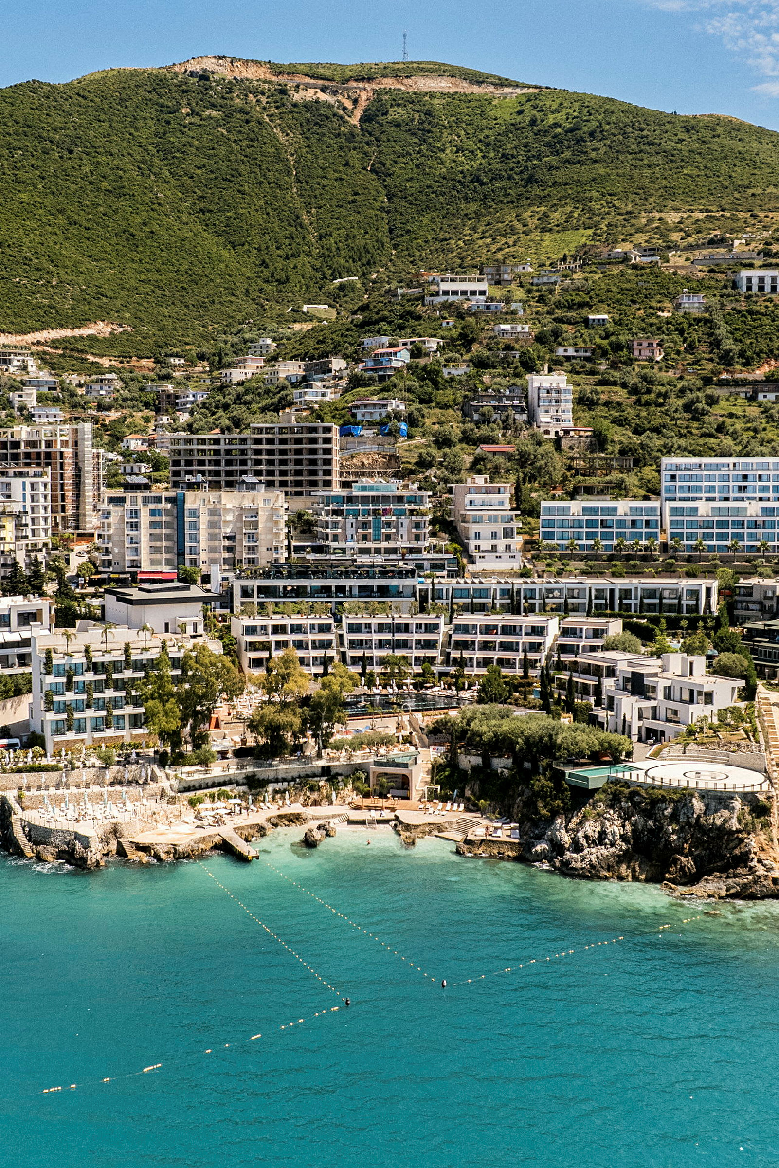 Vy över ett kustlandskap med hotellbyggnader och gröna berg i bakgrunden. (AI-genererad text)