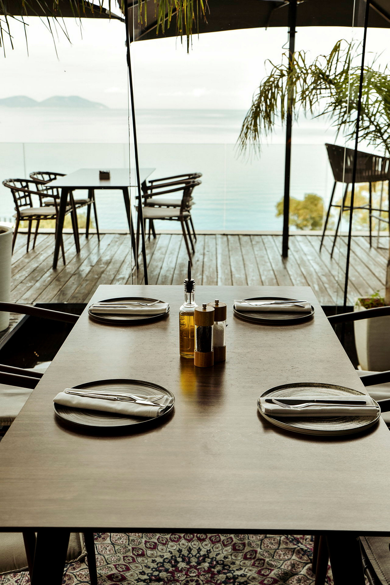Ett dukat bord med fyra tallrikar och bestick på en altan med utsikt över havet. (AI-genererad text)