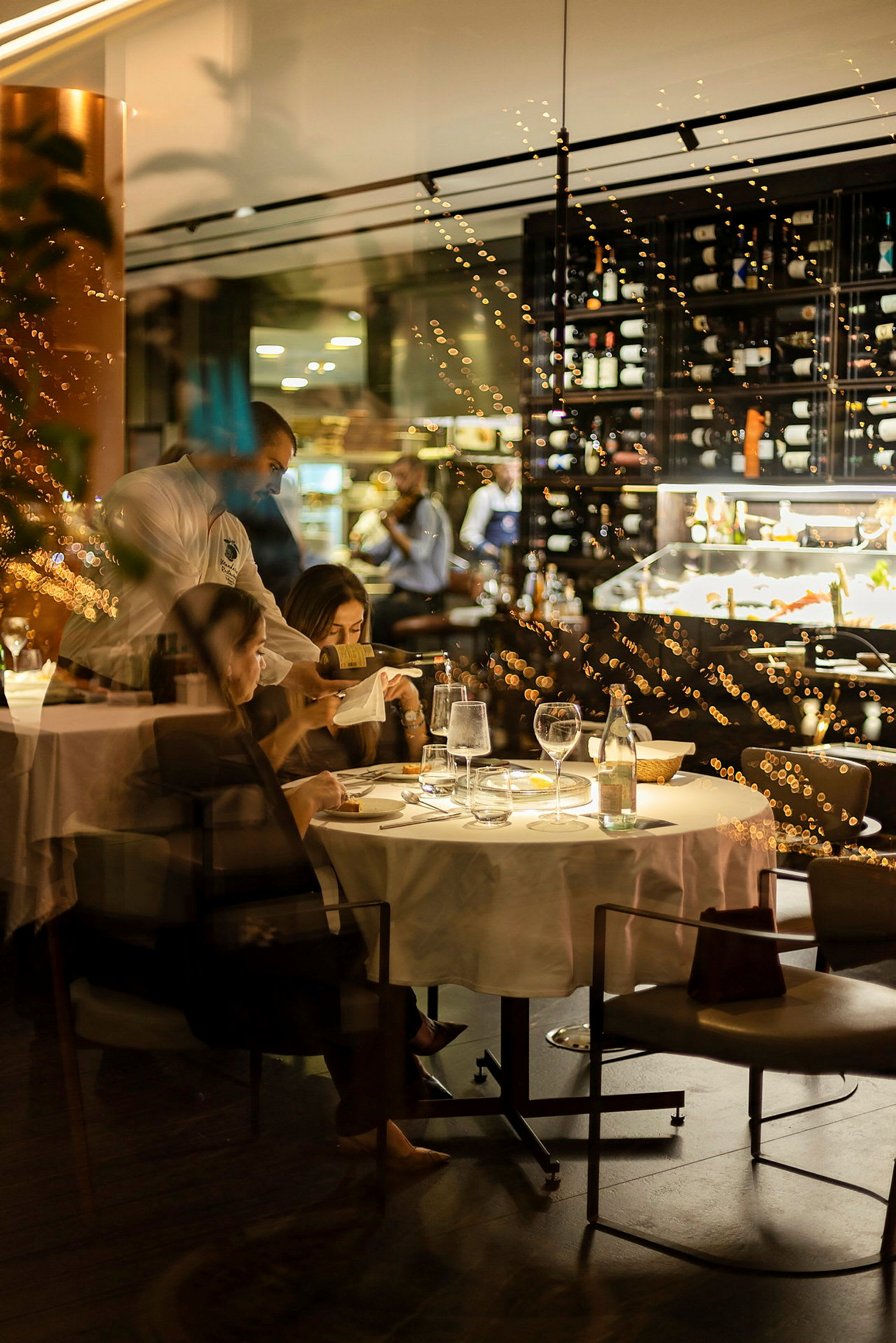 En restaurang med ett bord dukat för måltid och en vinhylla i bakgrunden. (AI-genererad text)
