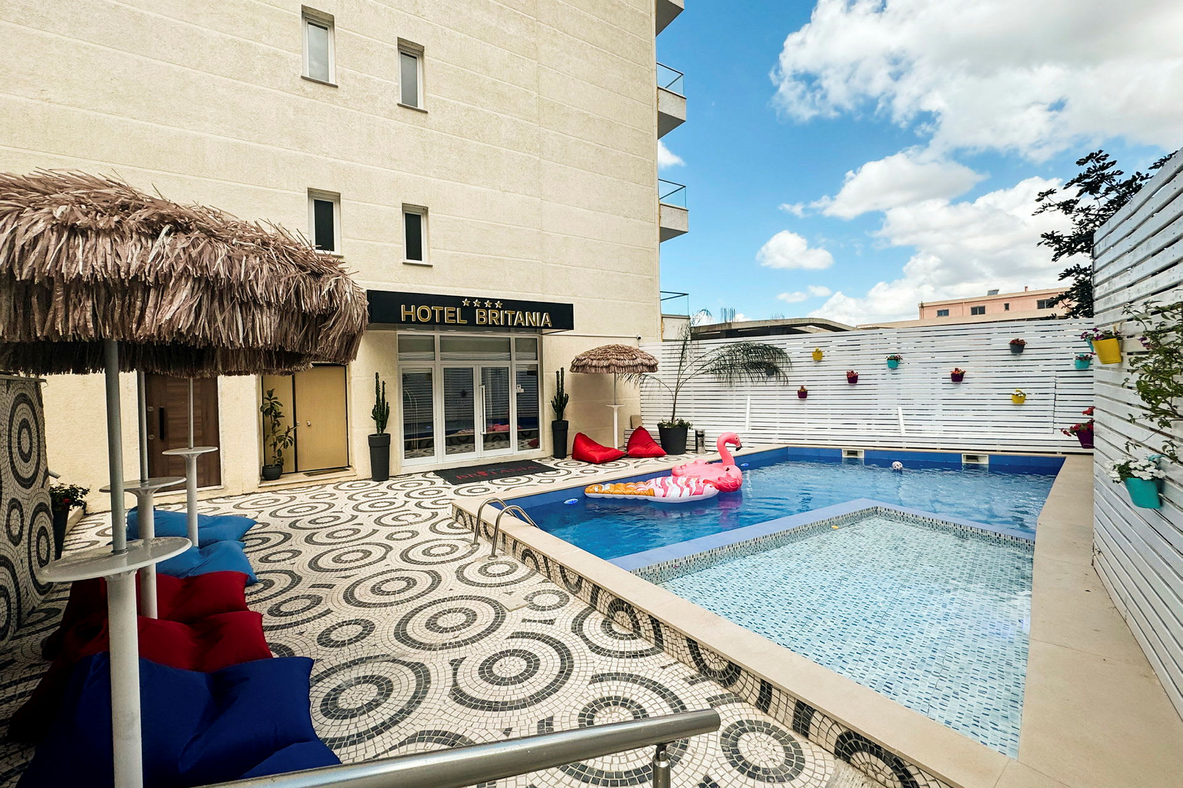Bild av en hotellpool med flytleksaker och dekorationer, omgiven av en uteplats med färgglada möbler och parasoller. (AI-genererad text)