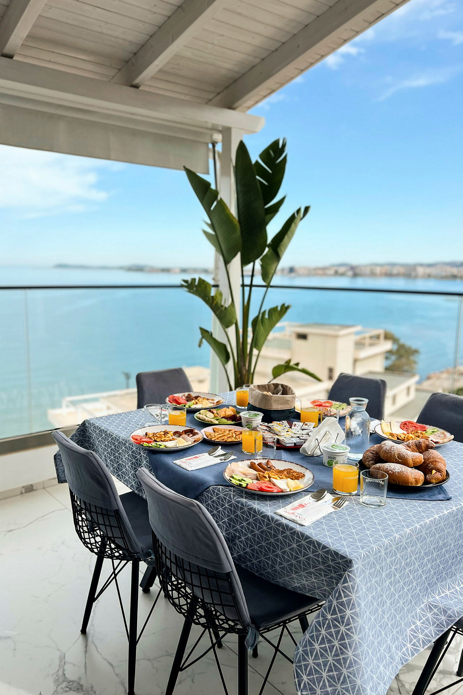 Ett dukat bord med frukost på en terrass med utsikt över havet. (AI-genererad text)