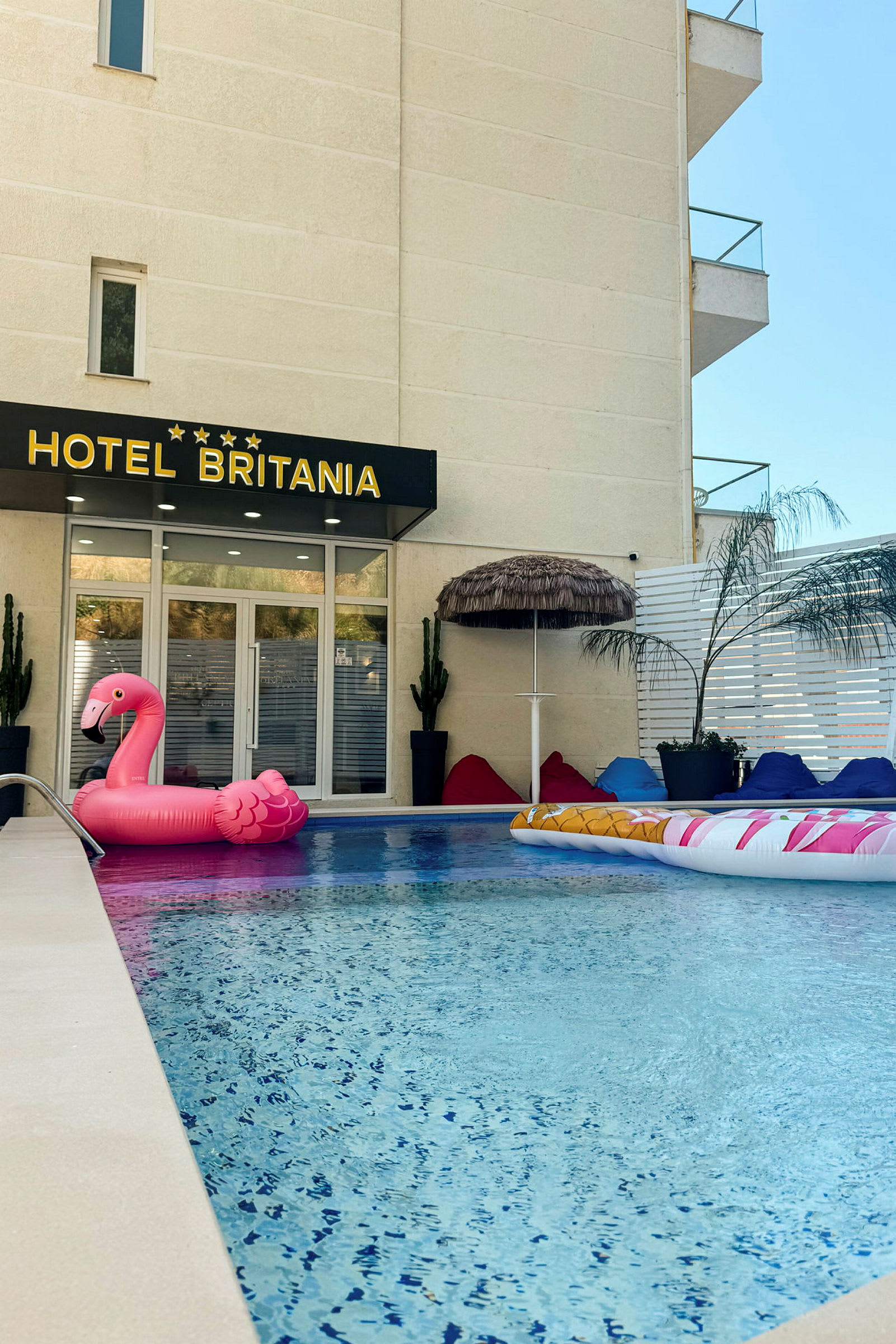 Hotellets poolområde med en rosa uppblåsbar flamingo och sittsäckar. (AI-genererad text)