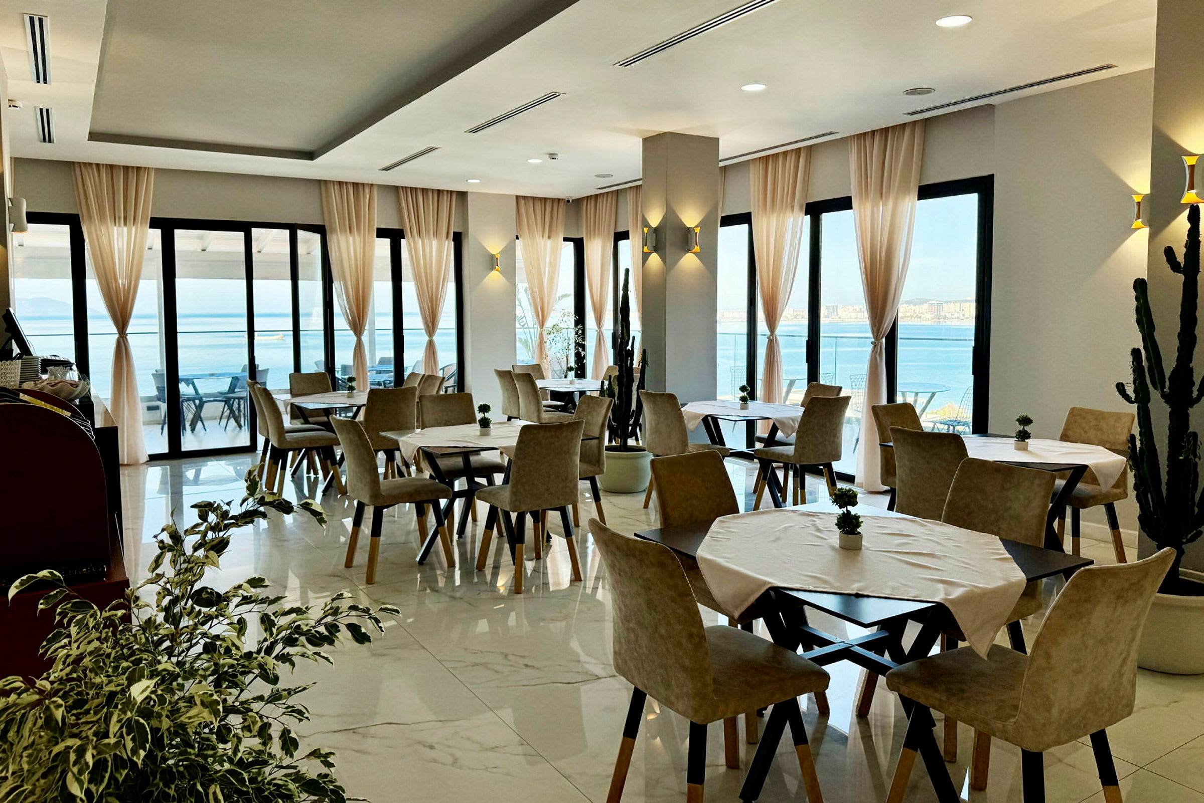 En restaurang med bord och stolar samt stora fönster med utsikt över havet. (AI-genererad text)