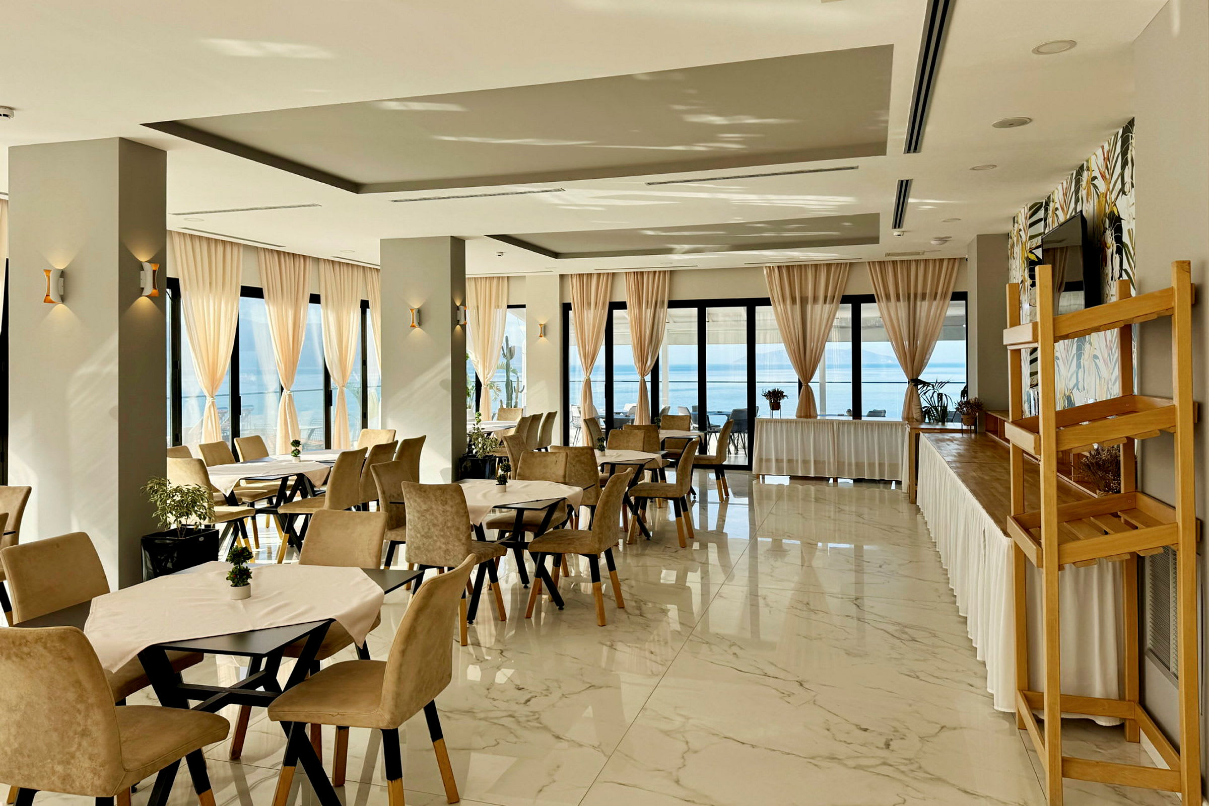 Restaurang med dukade bord och beige stolar, stora fönster med ljusa gardiner och havsutsikt. (AI-genererad text)