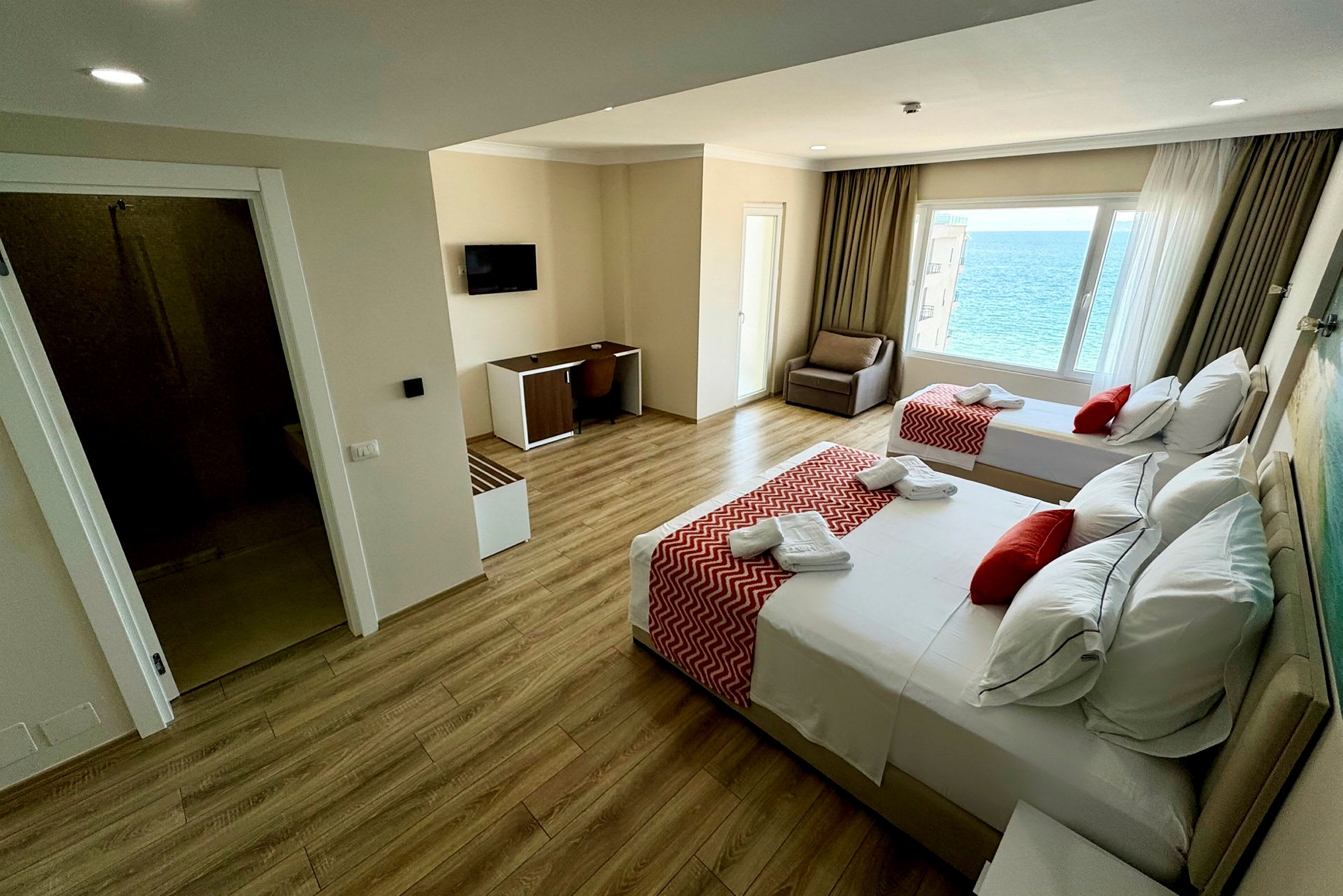 Hotellrum med två sängar, röd dekor och havsutsikt från fönstret. (AI-genererad text)