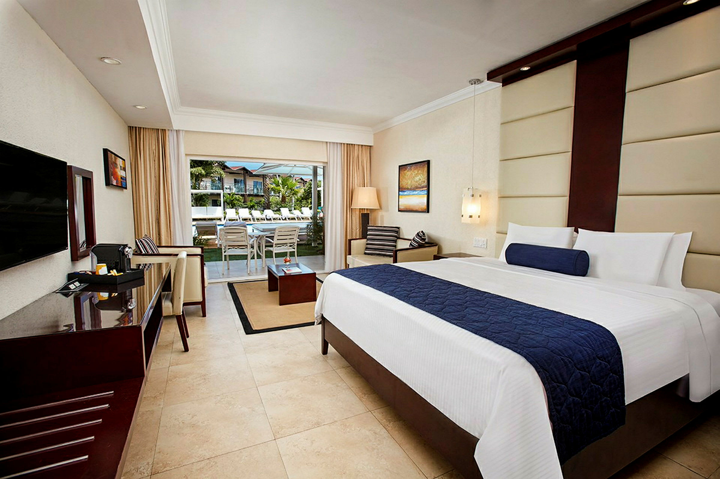 Hotellrum med modern inredning, dubbelsäng, sittgrupp och öppning mot en terrass med utsikt över en pool. (AI-genererad text)