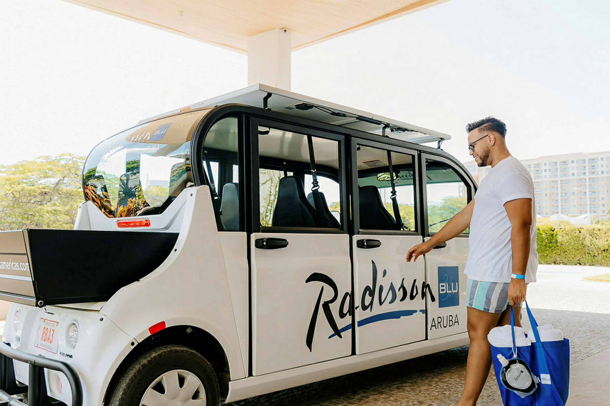 En turist står bredvid en vit transportbil med texten 'Radisson Blu Aruba'. (AI-genererad text)