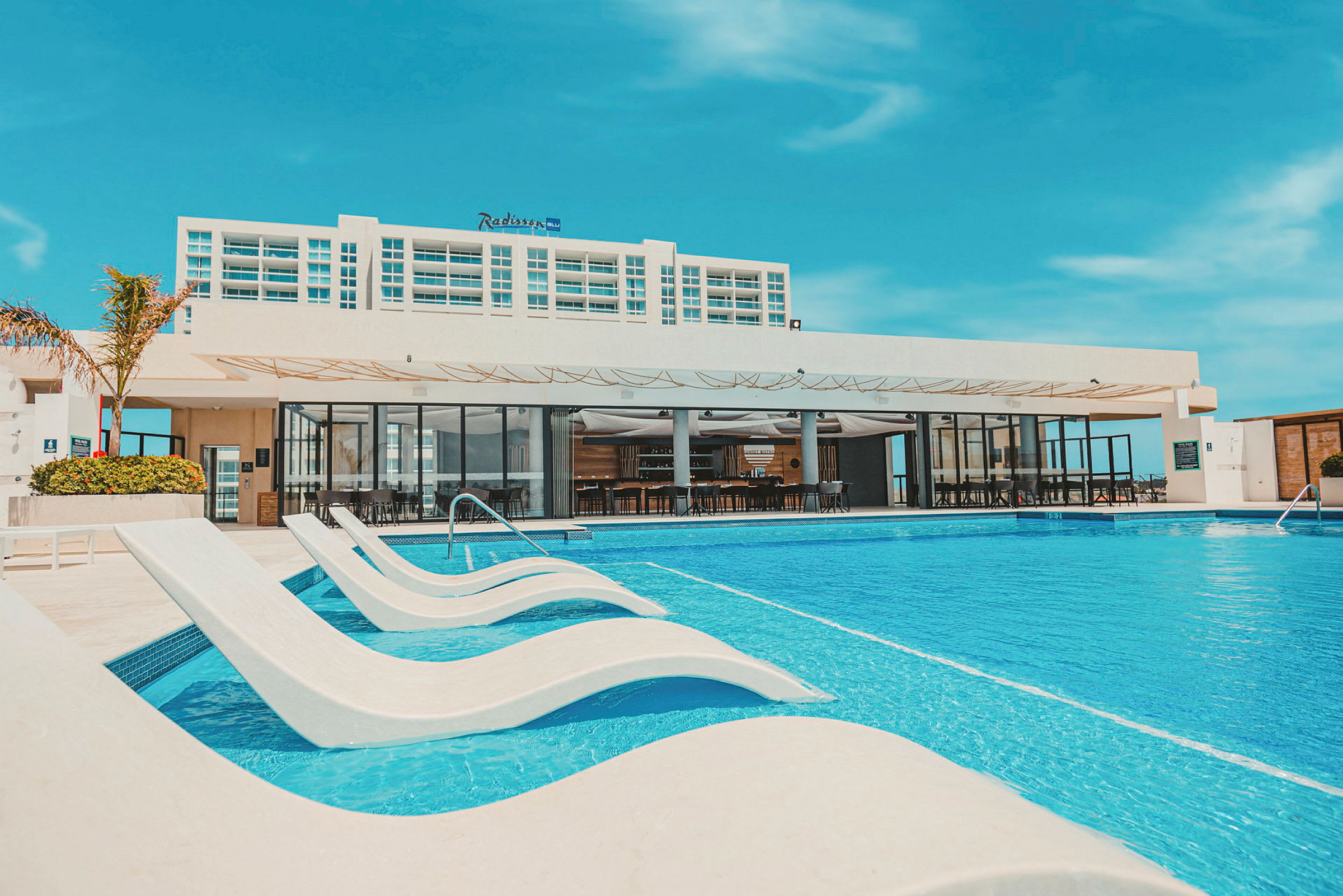 Utomhuspool med solstolar och en modern hotellbyggnad i bakgrunden. (AI-genererad text)