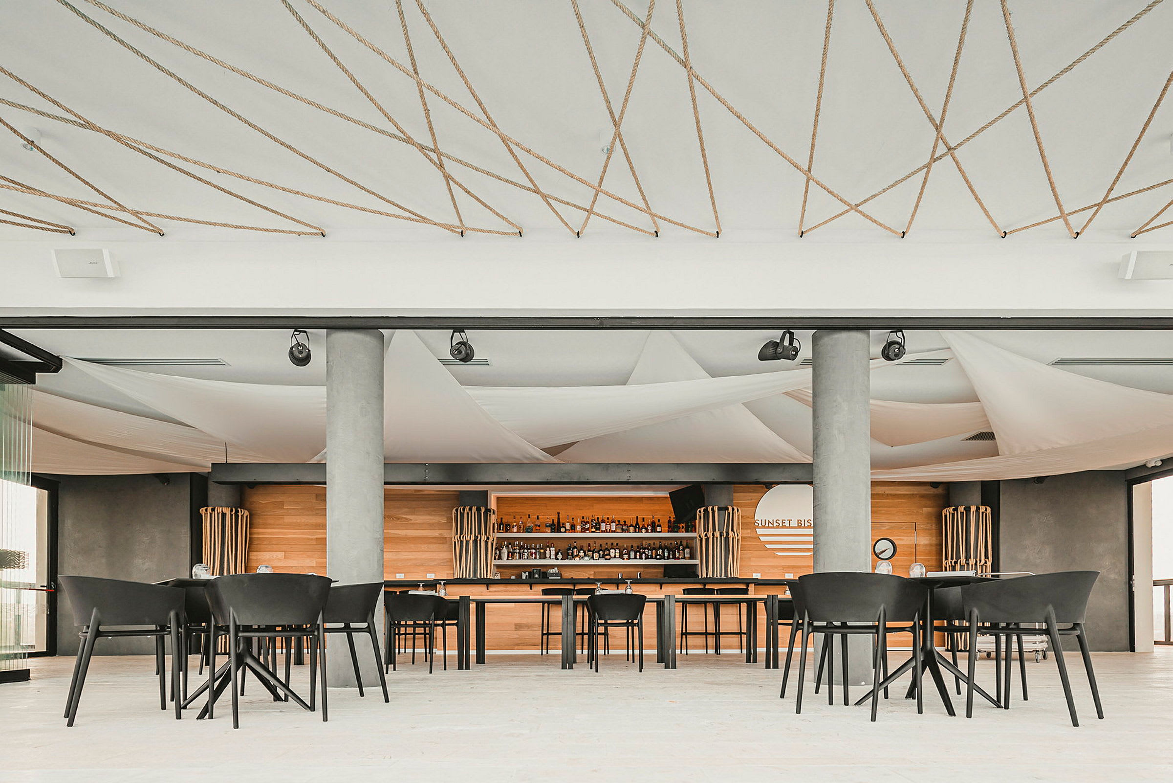 Ett café med moderna stolar och bord, träpaneler på väggar och dryckesutbud bakom bardisken. (AI-genererad text)